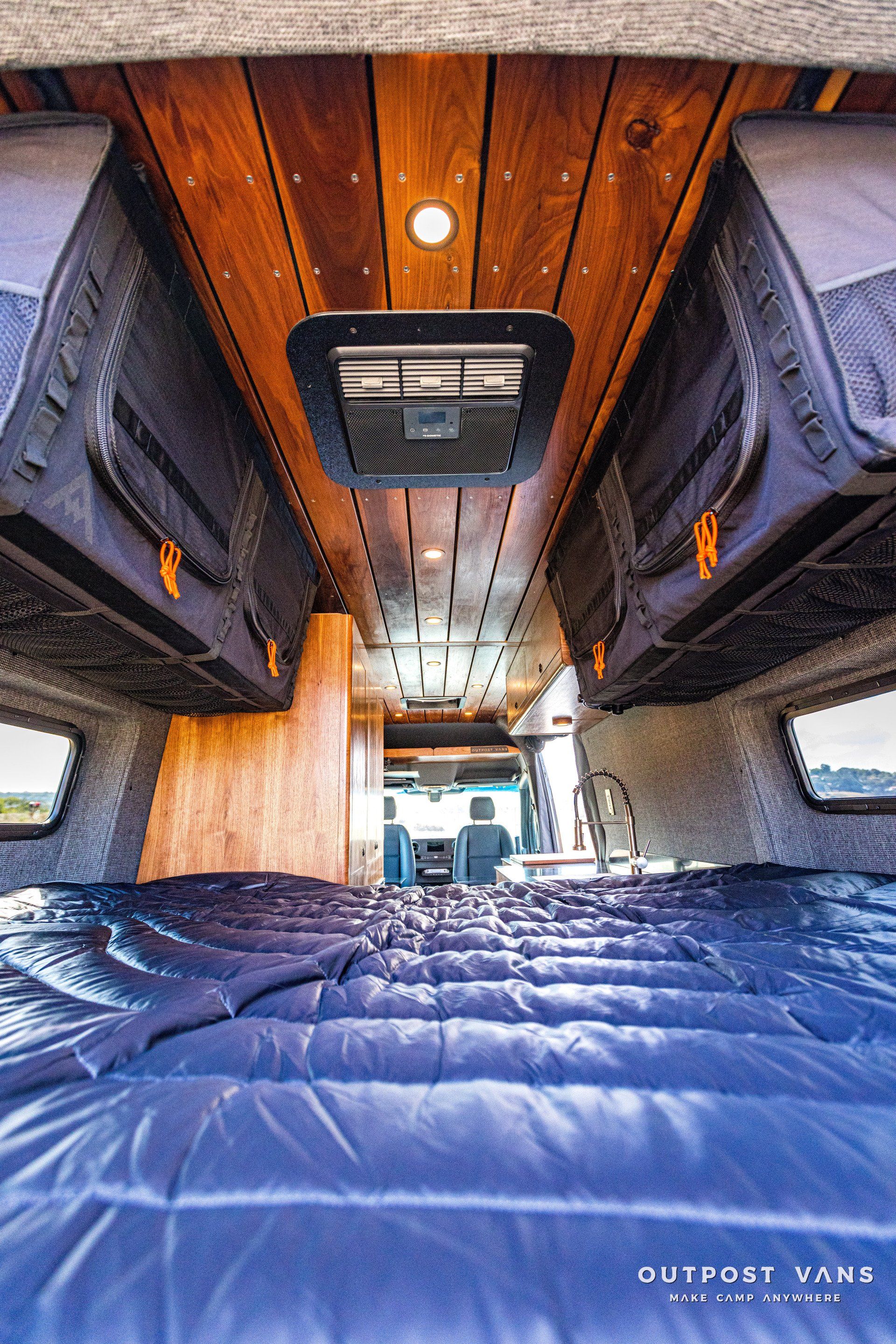 The inside of a van with a bed and a fan on the ceiling.