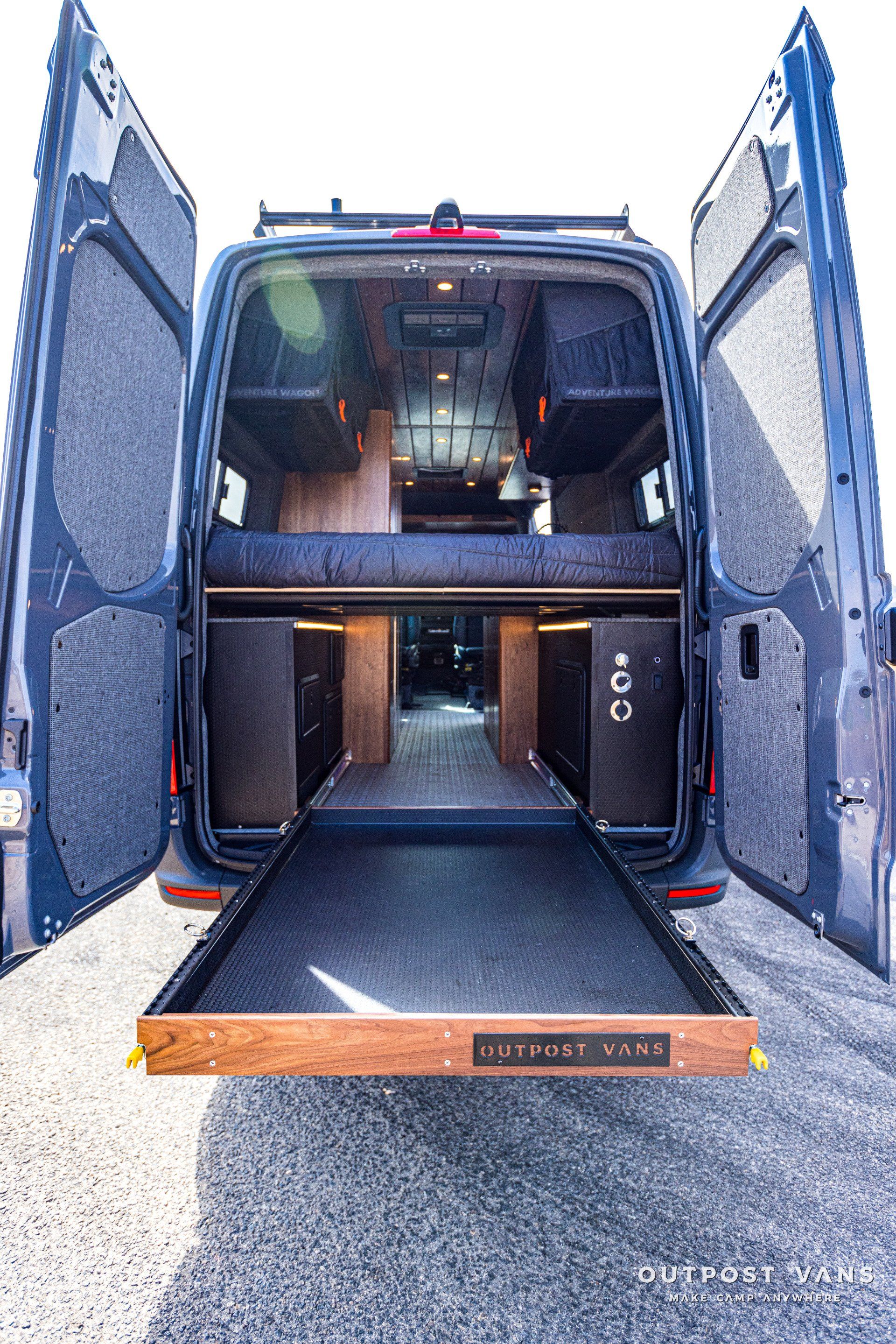 The back of a van with its doors open and a bed in the back.
