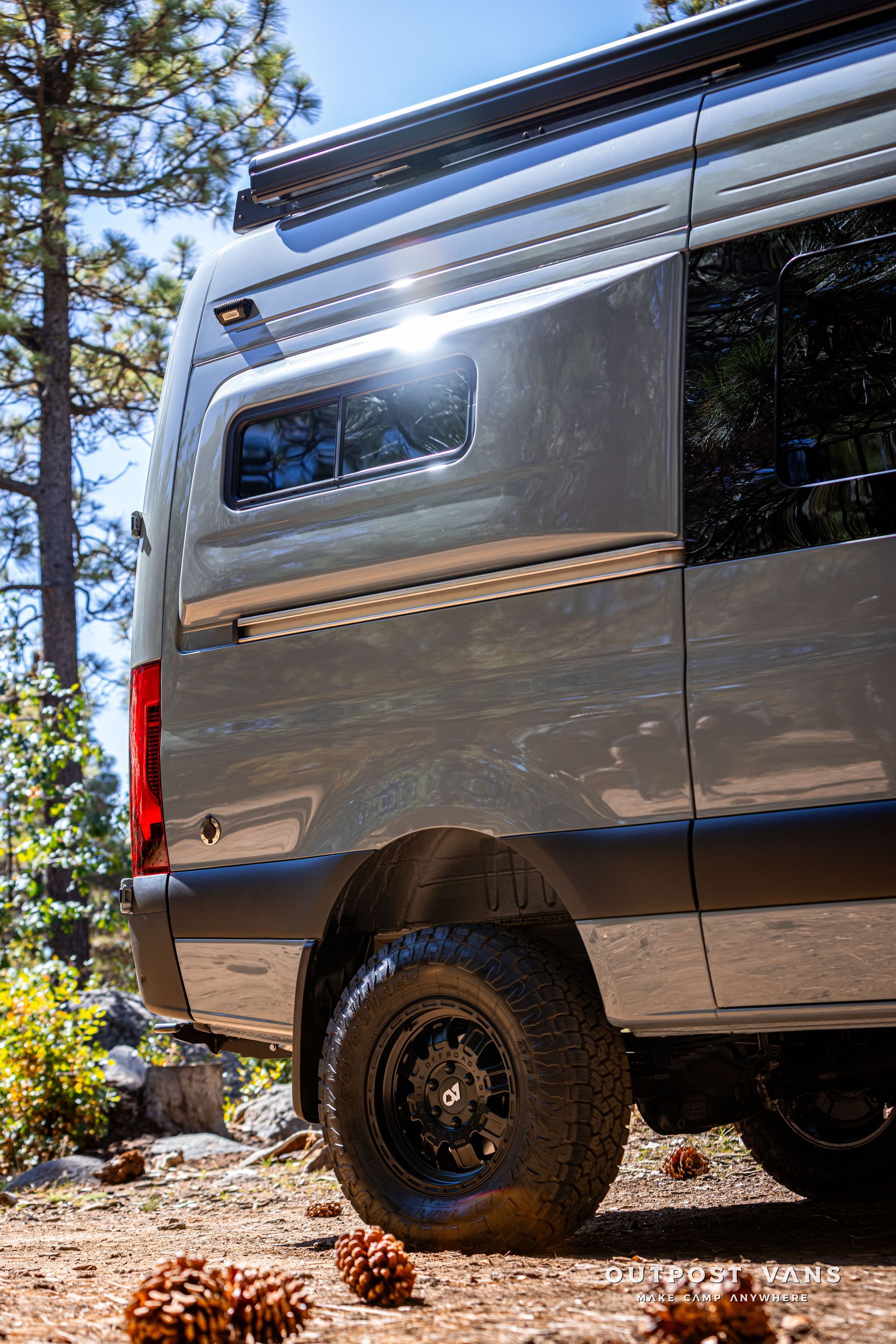 Sprinter Gray camper van with black tires on a dirt path, in a forest setting.