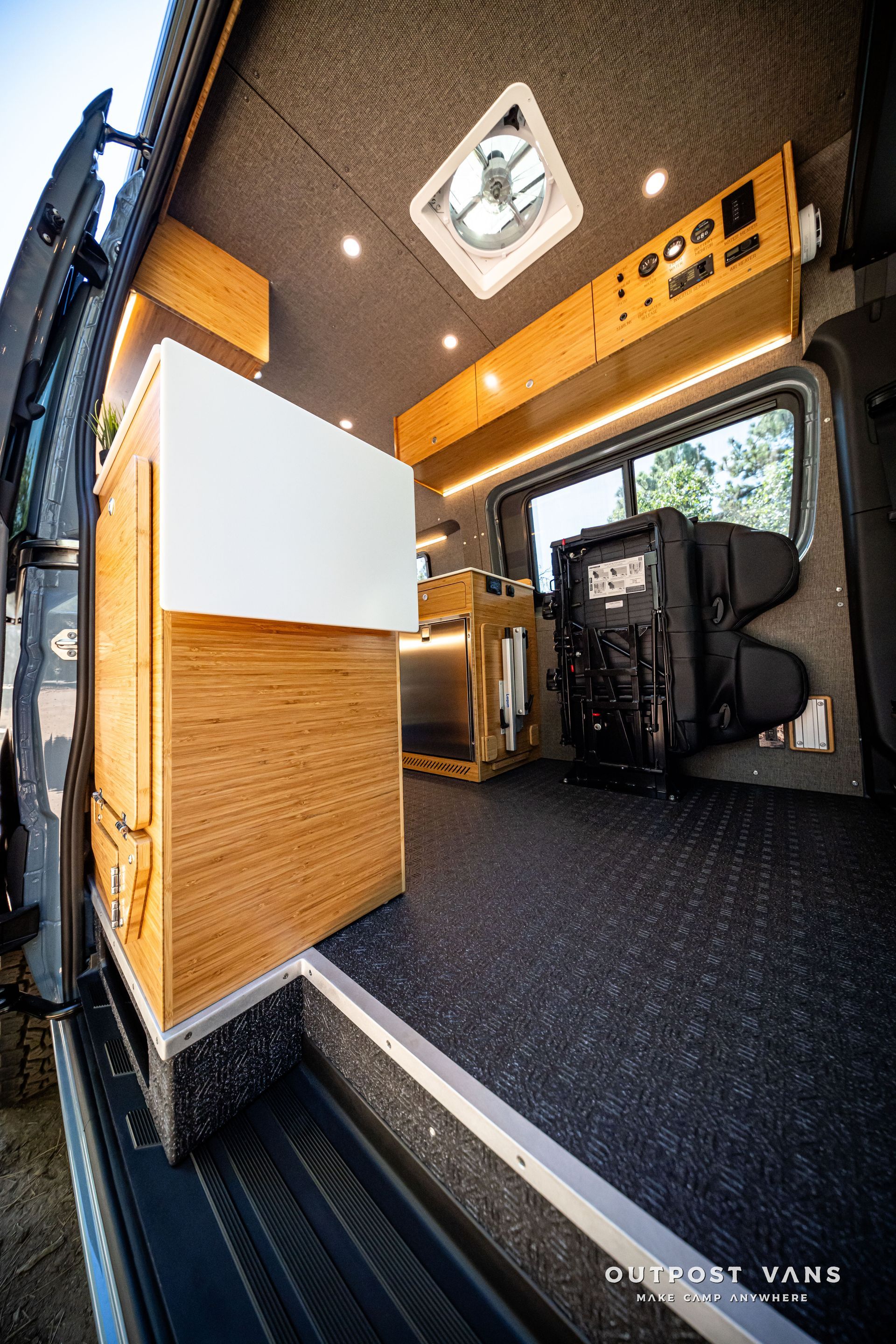 Sprinter Interior of a converted van with wood cabinetry, black flooring, and a fan in the ceiling.