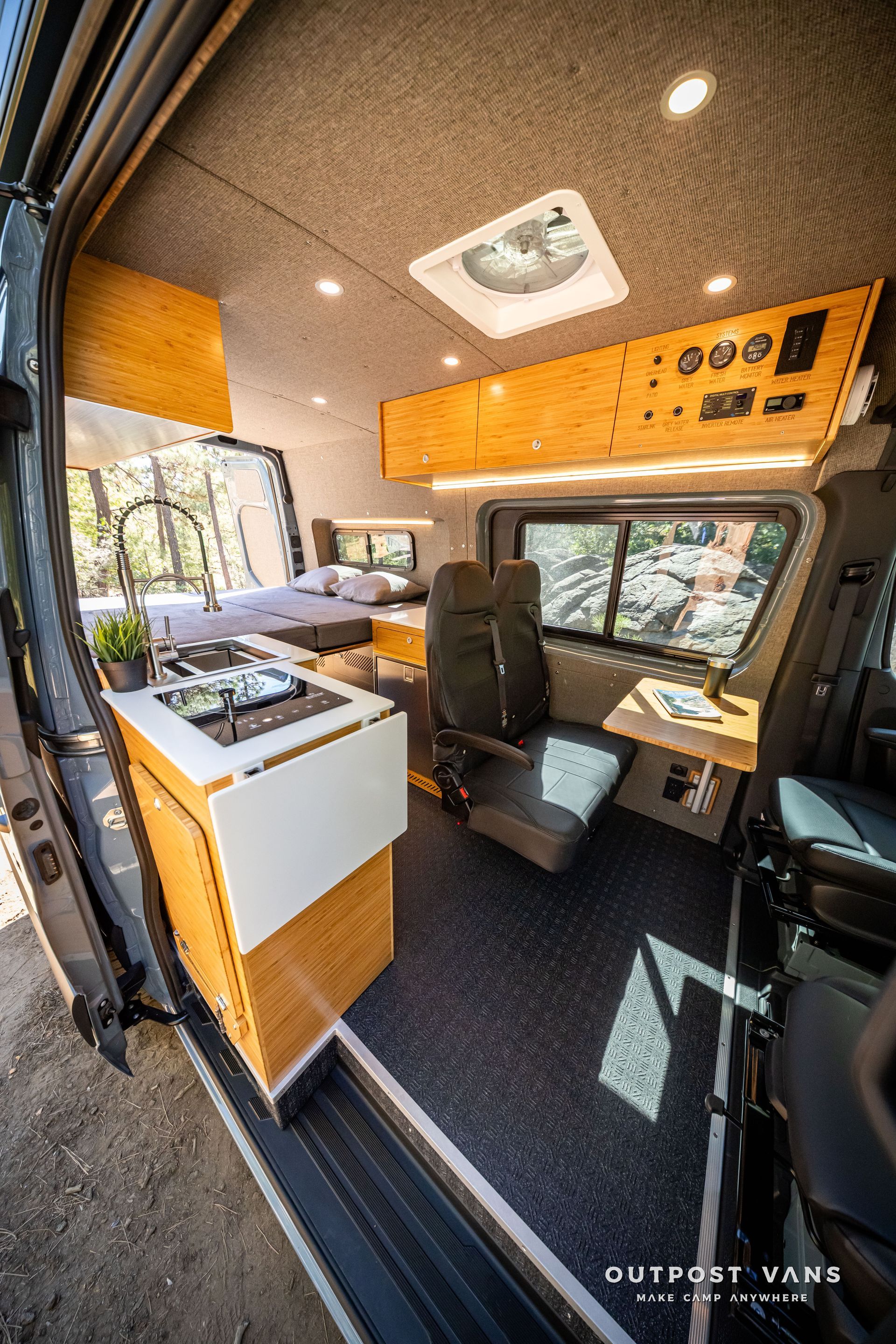 Sprinter Interior of a camper van with wood paneling, a bed, desk, and seating, with a sunny outdoor view.