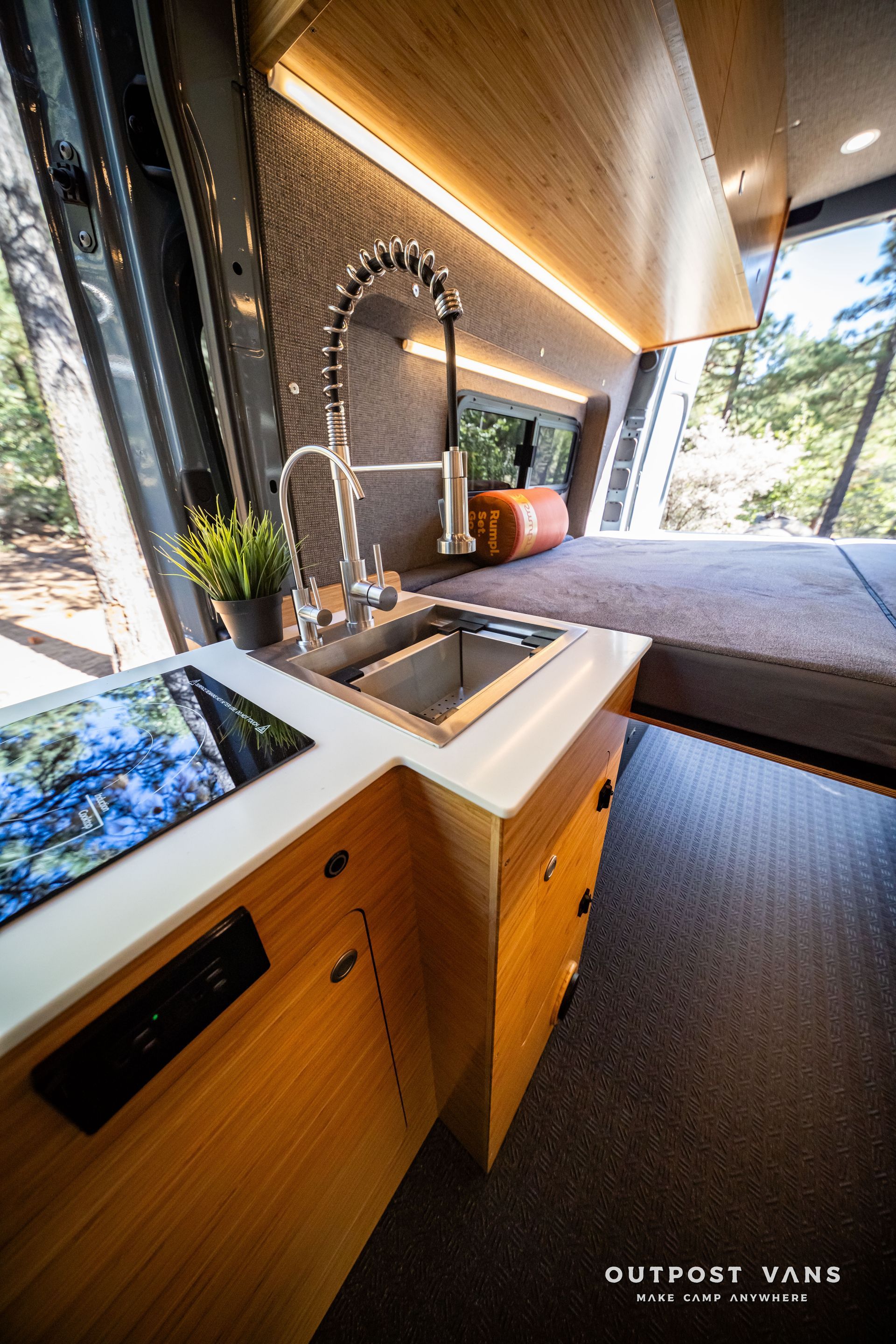 Sprinter Modern camper van interior with kitchen, bed, and large windows overlooking trees.