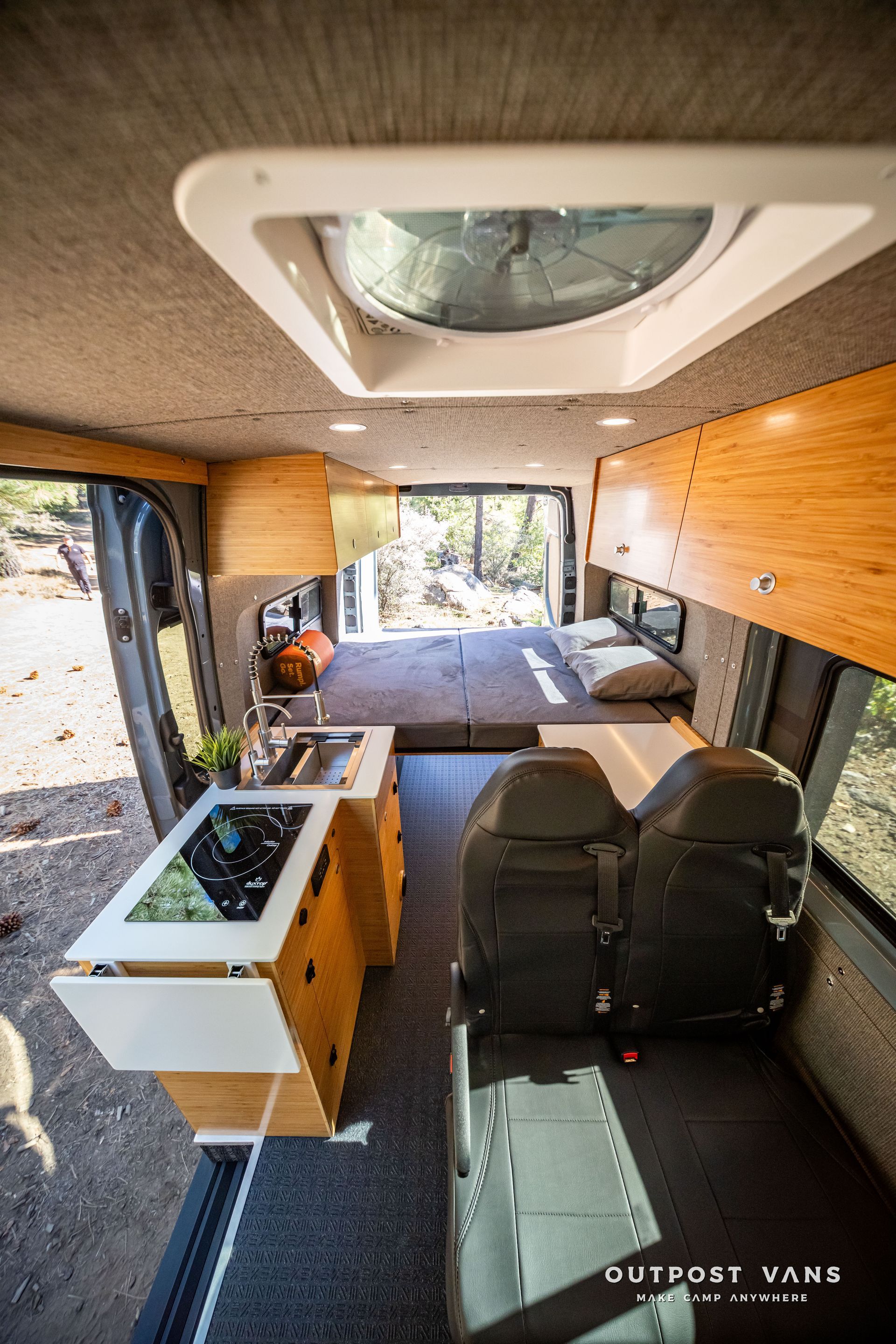Sprinter Interior of a camper van with kitchen, bed, seating, and open back doors; wood and neutral colors.