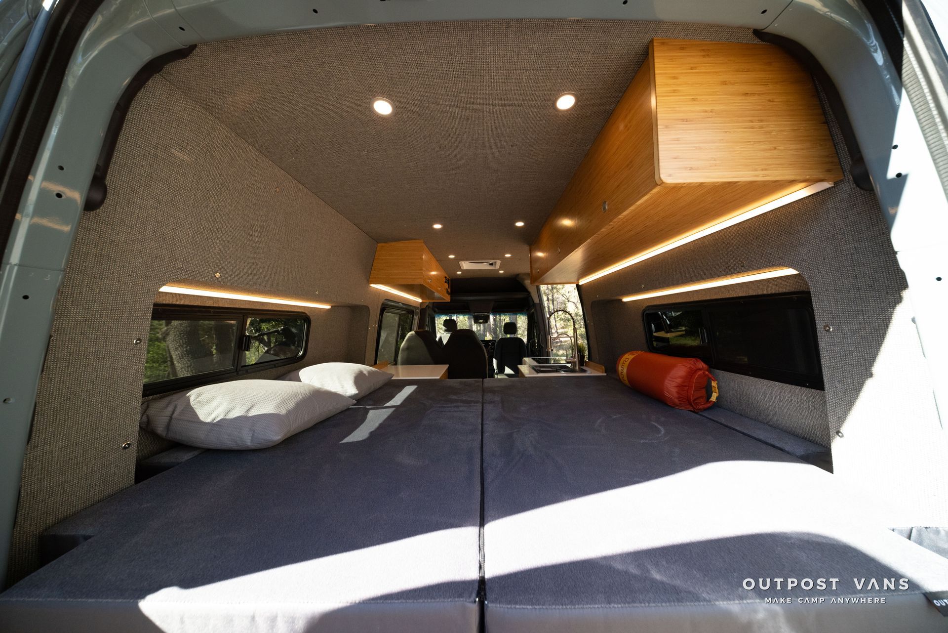 Sprinter Interior view of a campervan with a large bed, overhead storage, and integrated lighting.