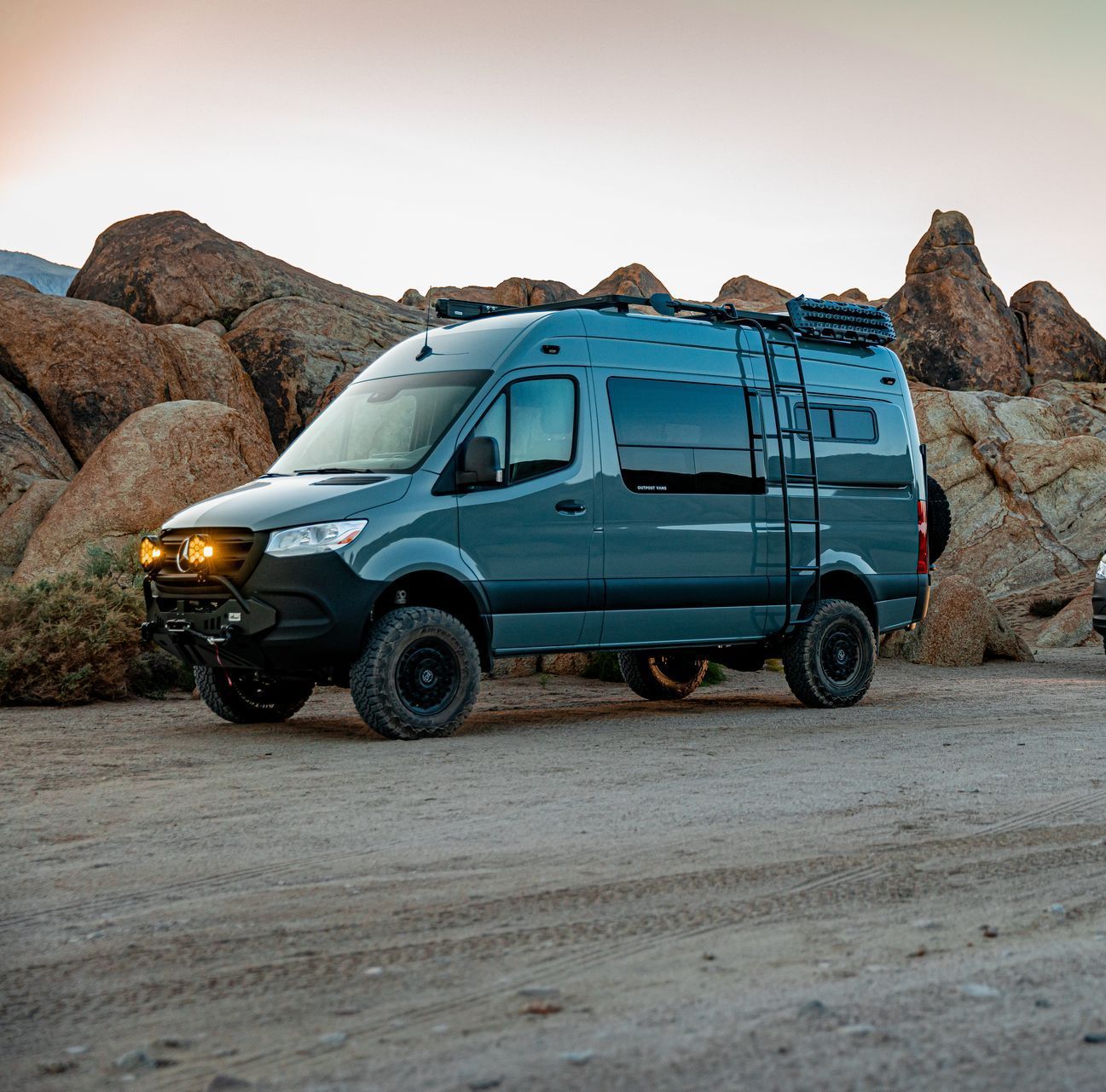 a blue van with a ladder on the roof is parked on a dirt road .