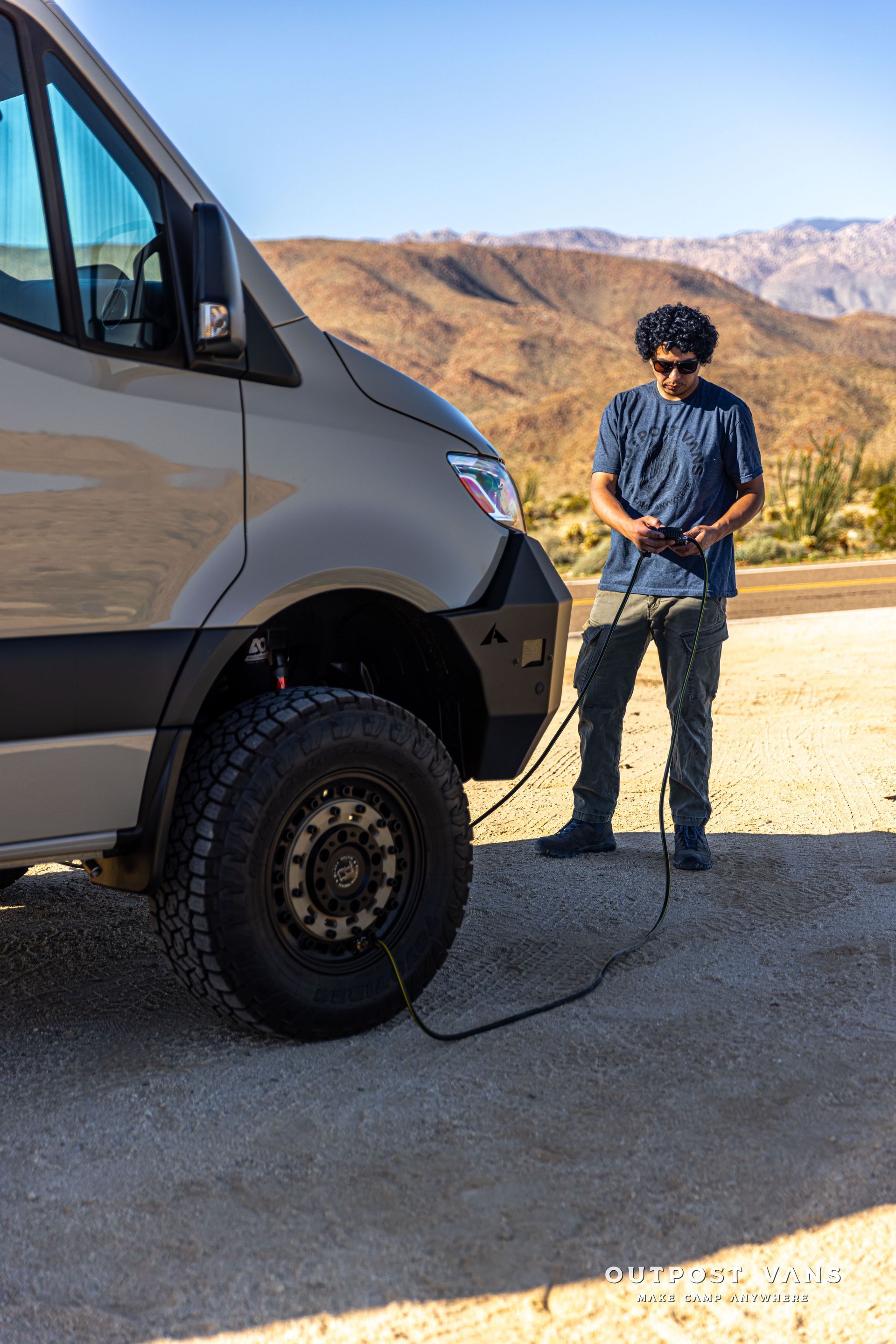 Person standing beside a van holding a cable in a mountain roadside setting