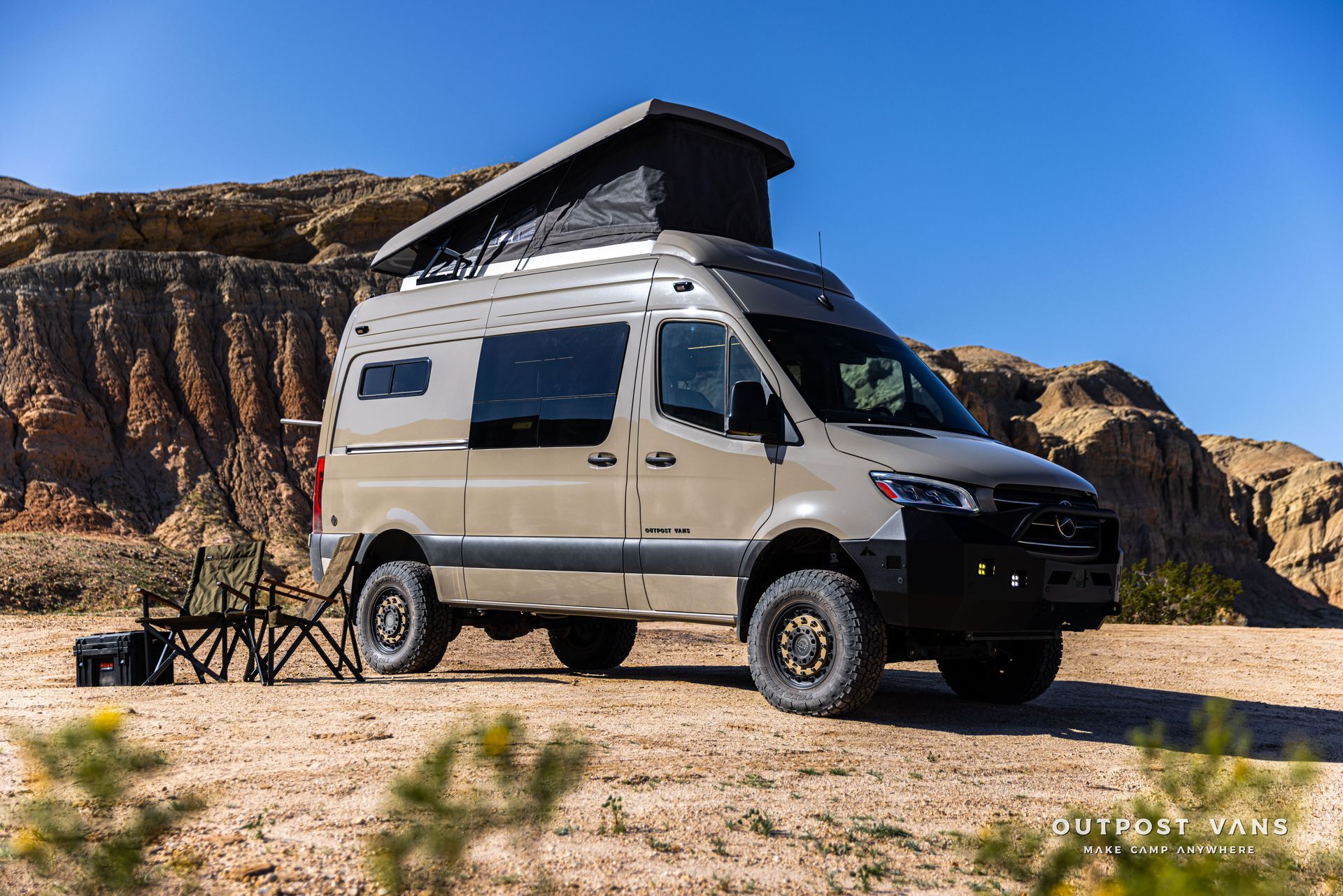 Beige off-road camper van parked in a rocky desert landscape under a blue sky.