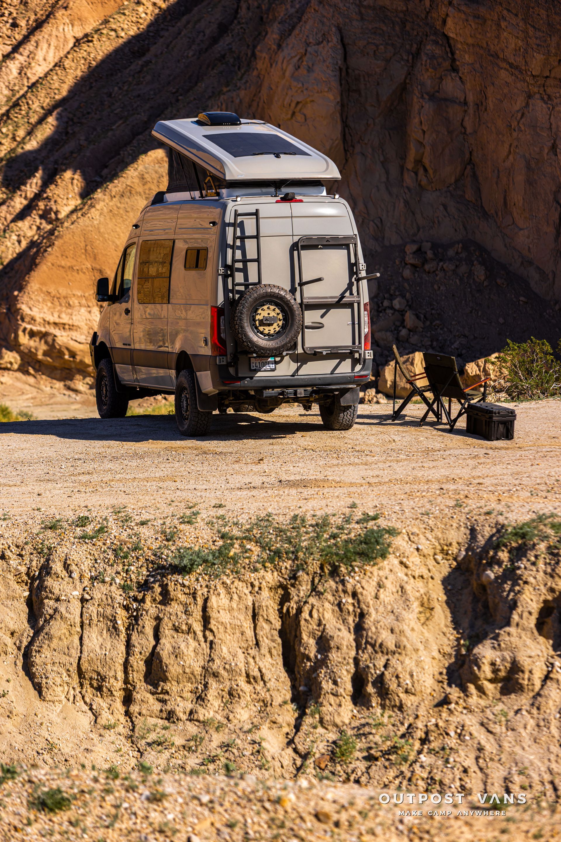 White camper van with rooftop tent parked on a rocky desert trail near a canyon wall
