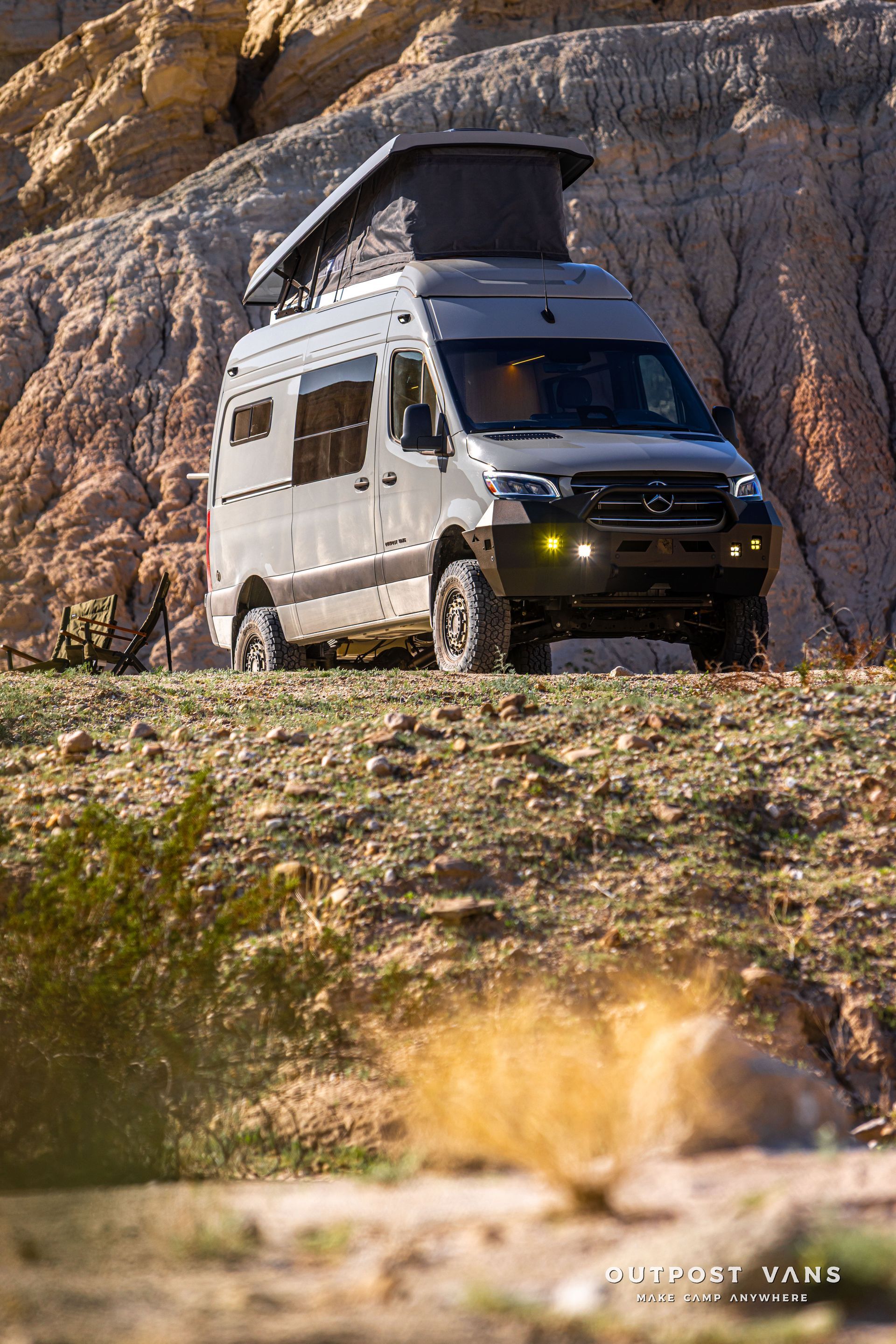 White off-road camper van on a rocky trail with a rooftop tent, set against a cliffside.