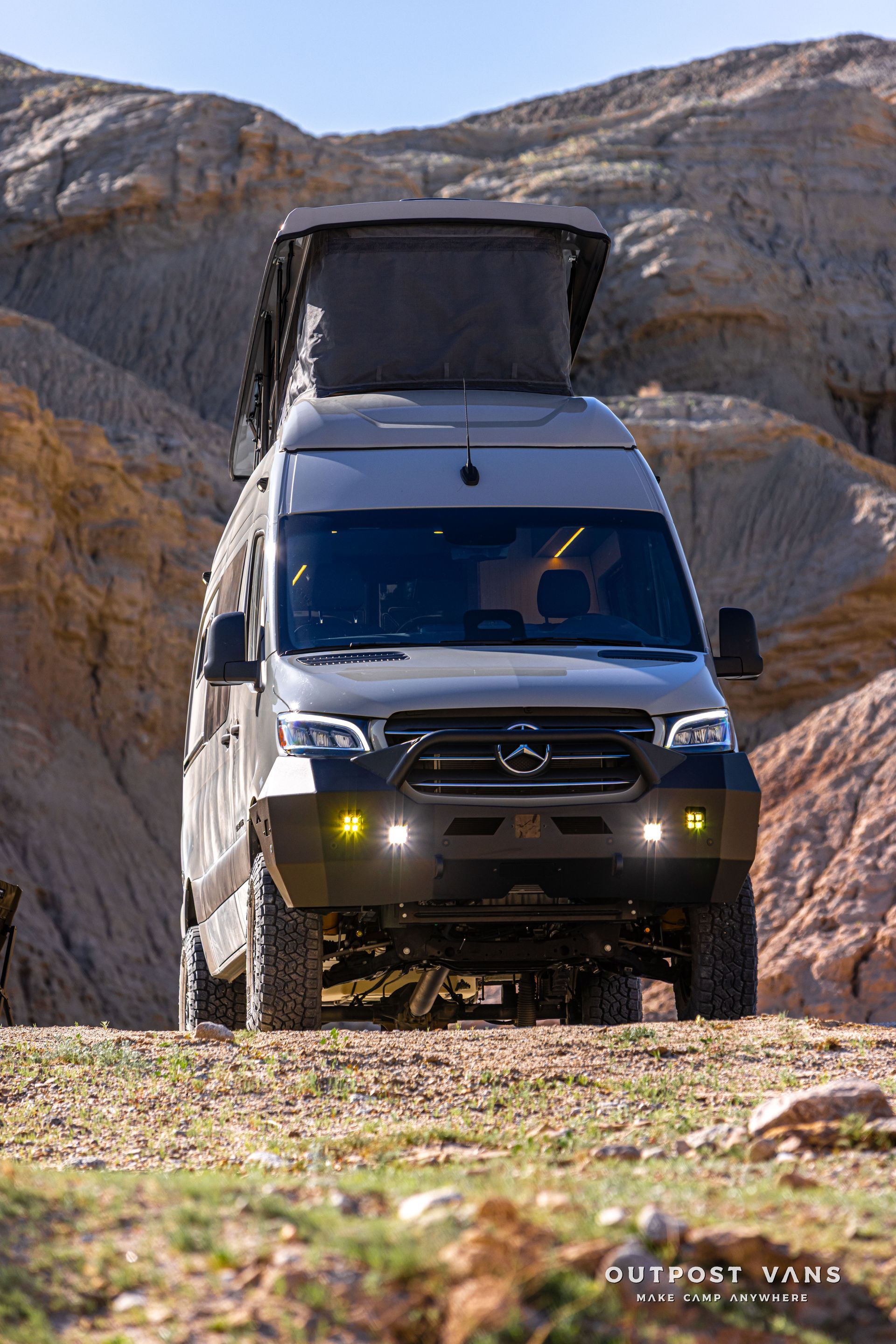 Black Mercedes camper van on a rocky off-road trail with a raised rooftop tent in a desert canyon