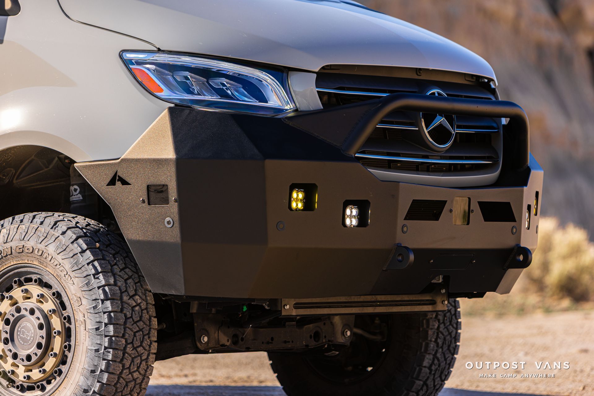 Front view of a silver off-road SUV with a black bumper and large rugged tires in a desert setting