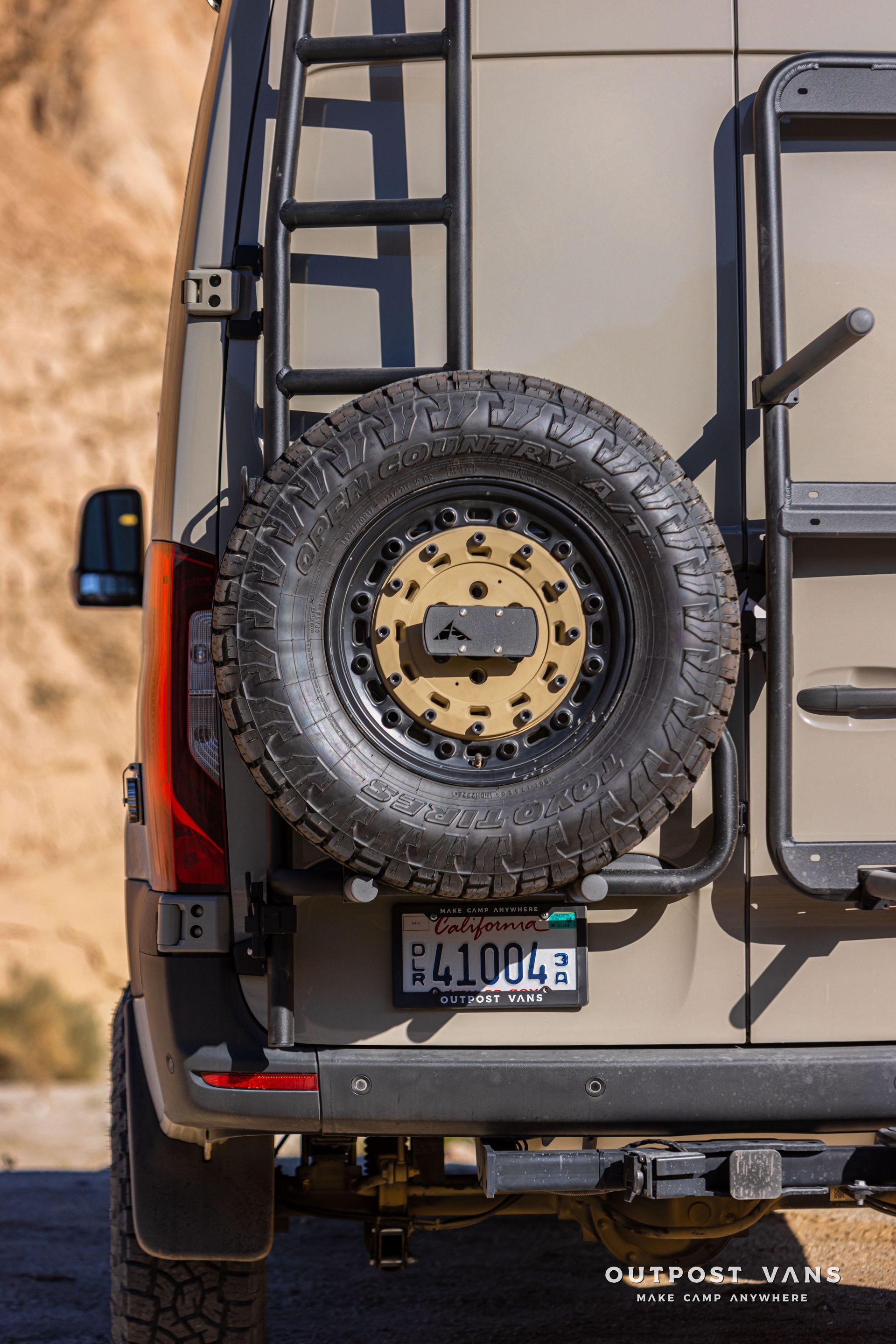 Rear view of a beige off-road SUV with a spare tire mounted on the back, parked on sandy terrain.