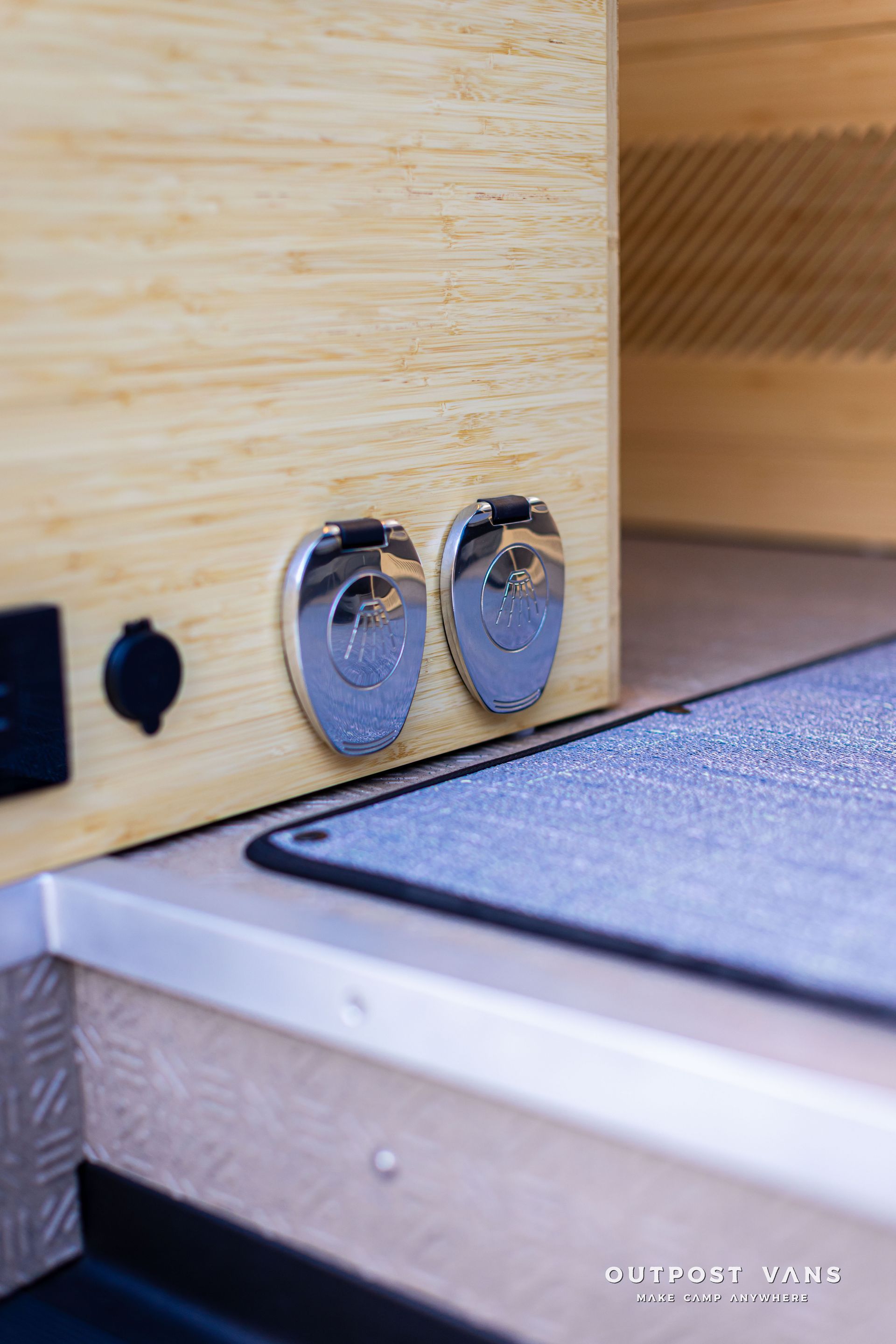 Close-up of two chrome knobs on a light wood cabinet beside a gray mat.