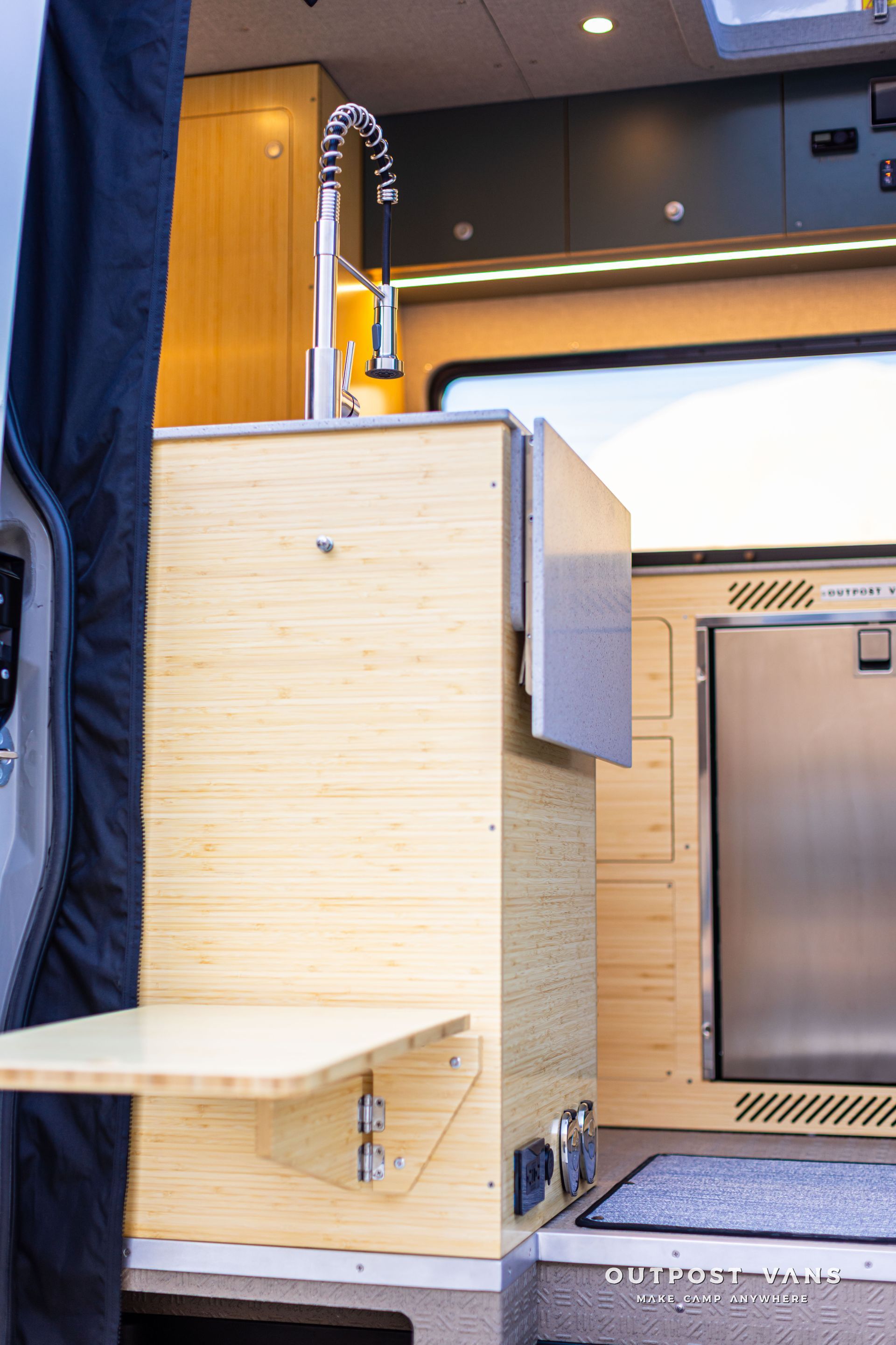 Compact wood-finished kitchenette and shower area inside a modern van interior.