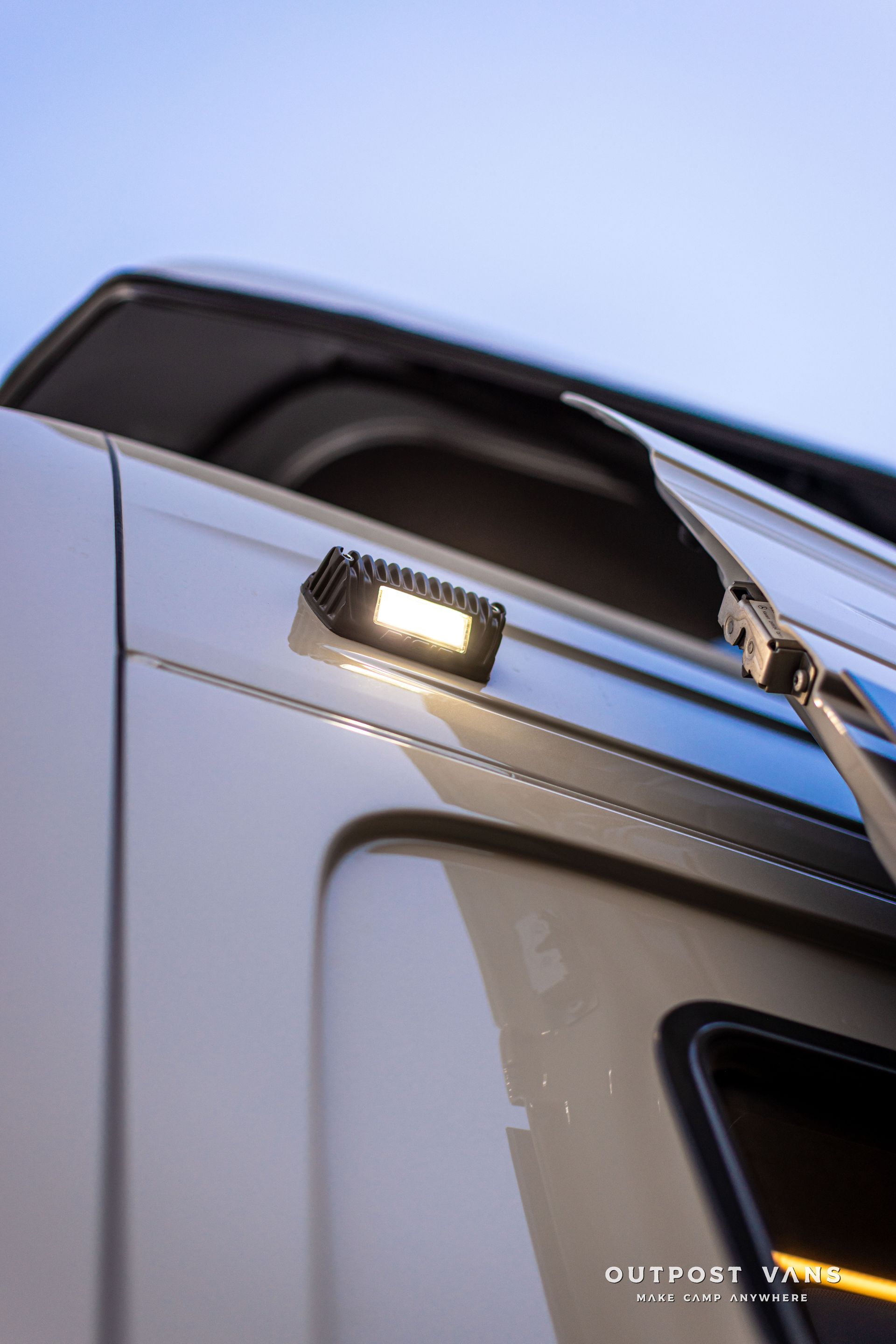 Close-up of a vehicle’s side mirror and lit door light against a blue sky