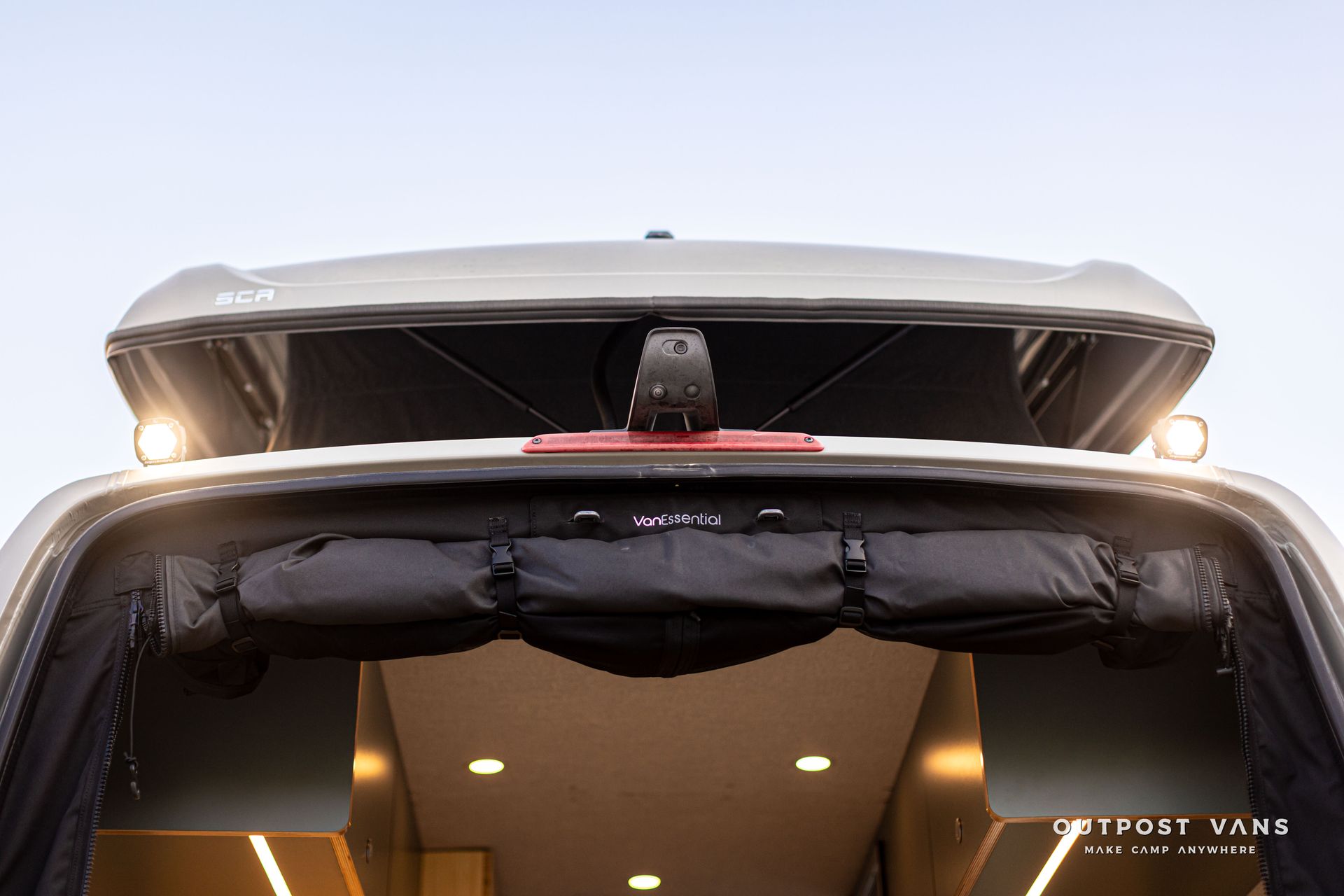 Front view of a white car with a rooftop light bar and windshield cover, headlights on