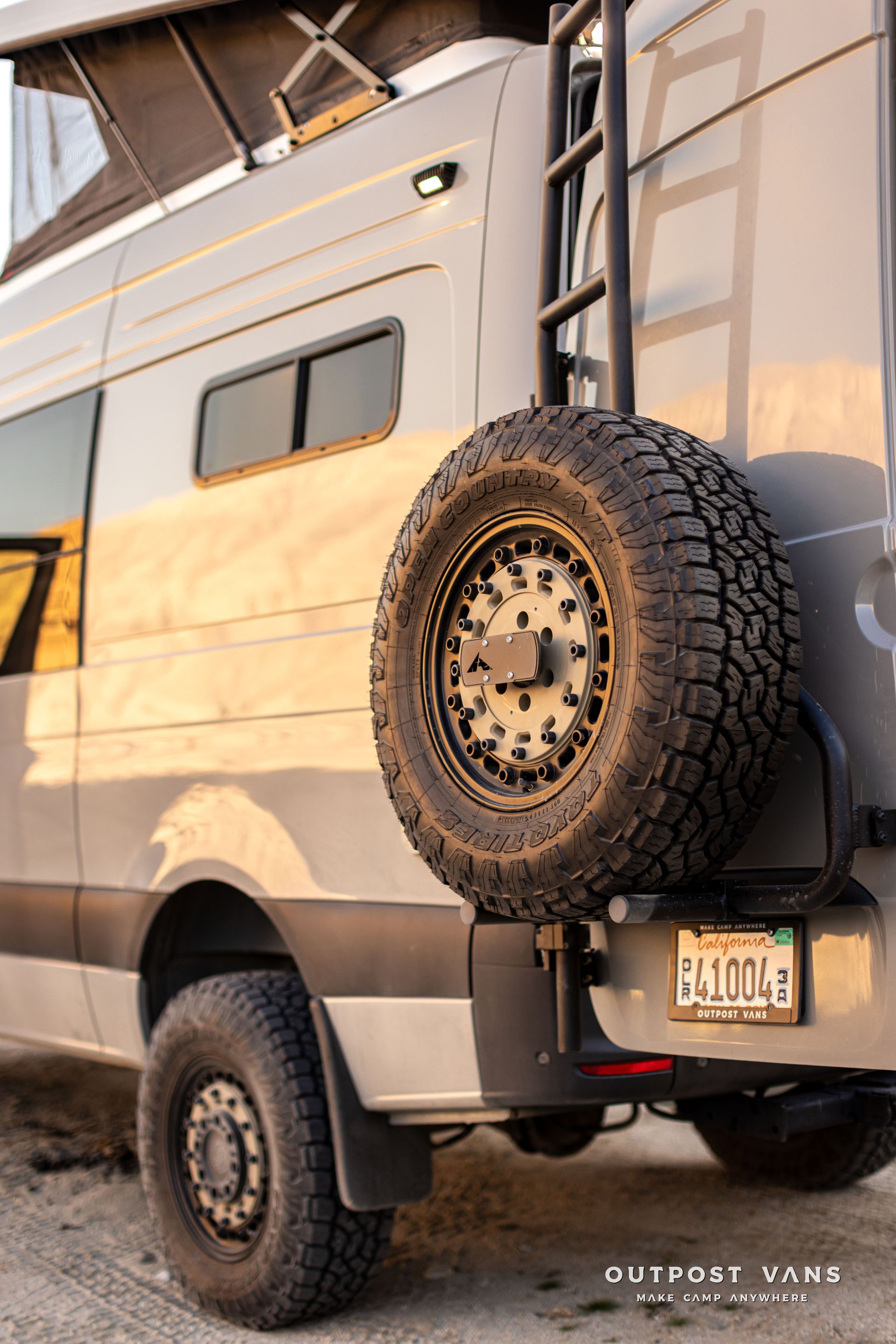 Off-road van with rear-mounted spare tire, parked outdoors at sunset