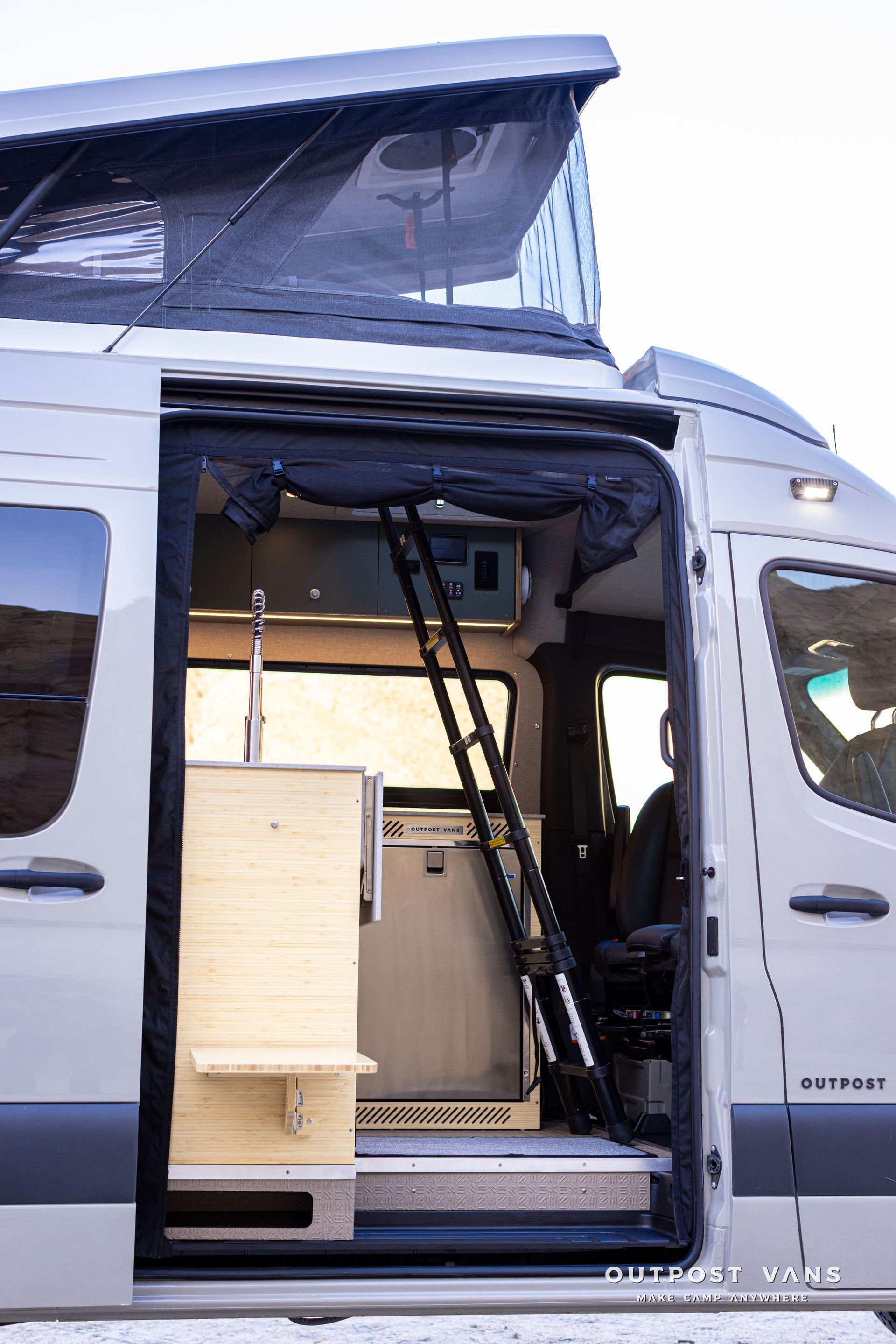Open camper van with raised roof and a wooden storage unit inside.