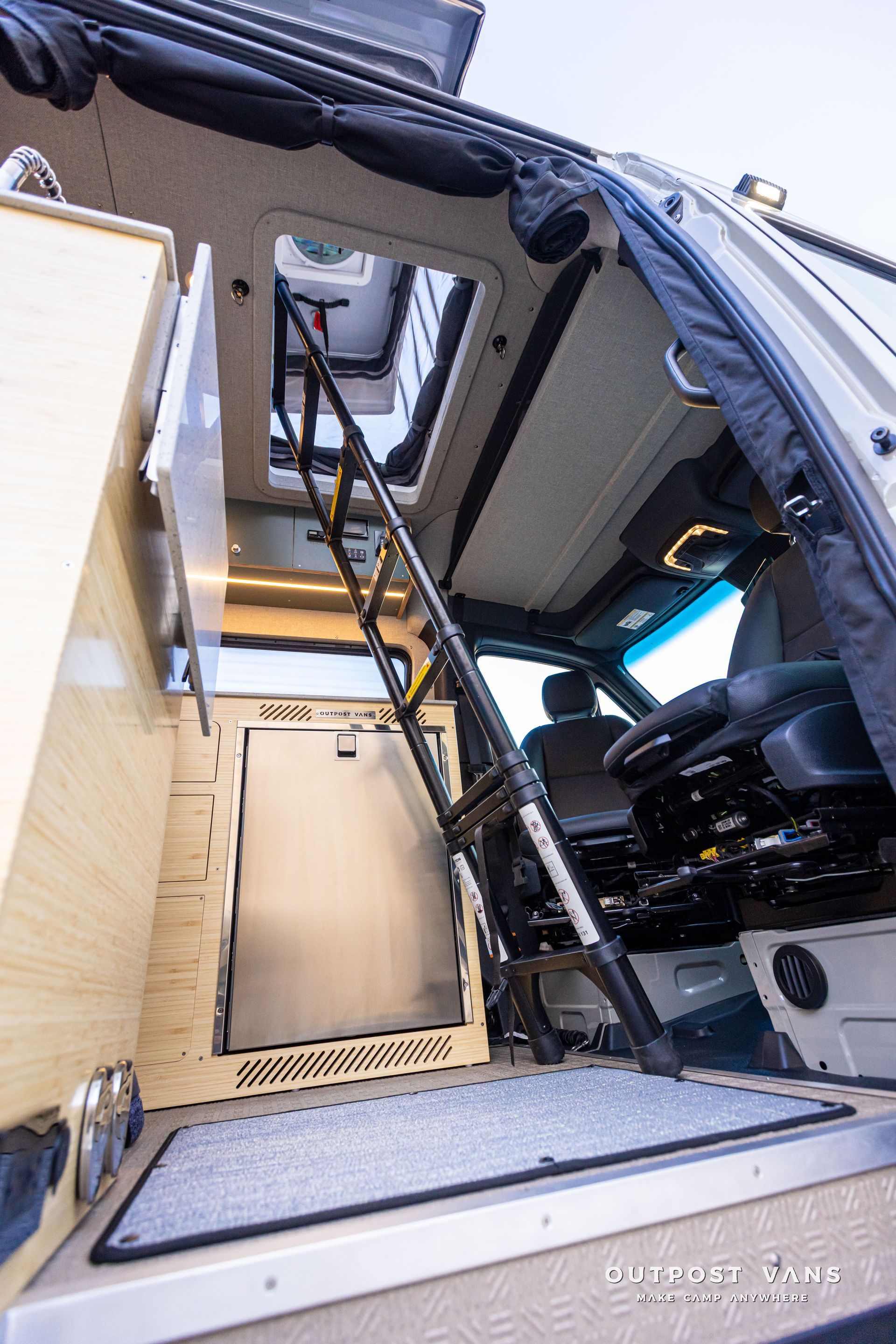 Open camper van interior with wooden storage cabinet, ladder, and front seats visible.