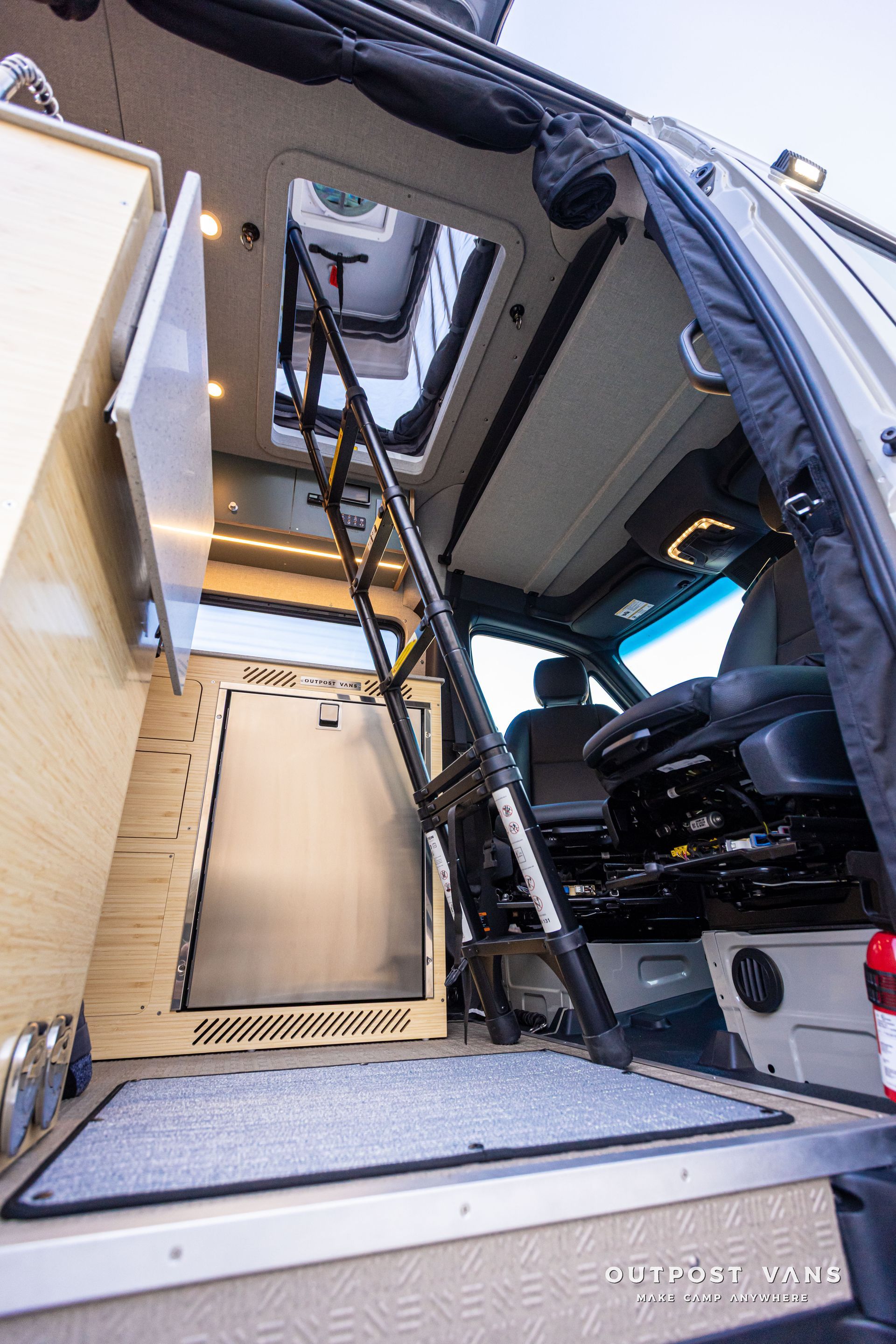 Camper van interior with open rear doors, built-in wood cabinetry, and a raised platform ceiling window