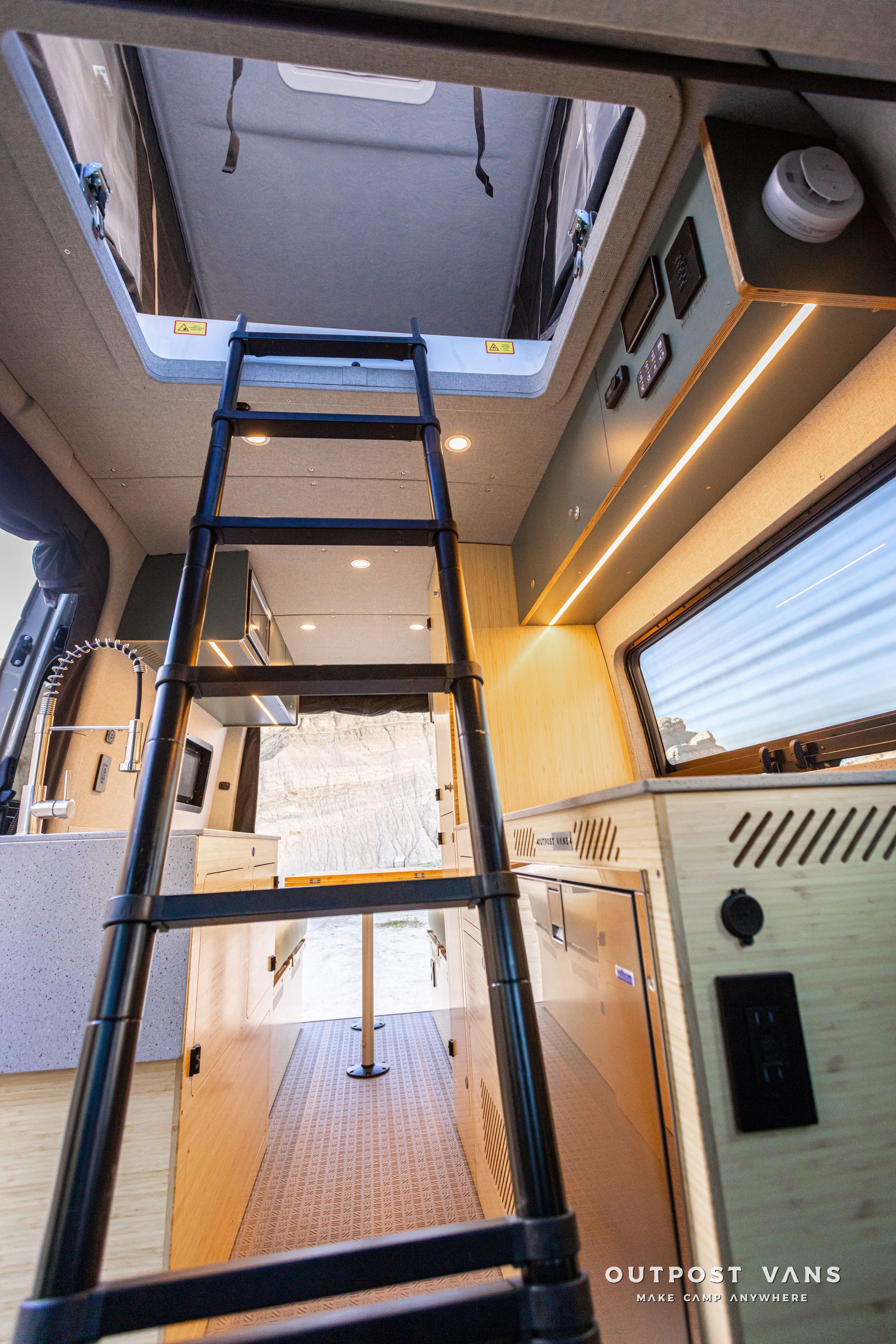 Interior of a camper van with a loft ladder, skylight, wood cabinetry, and a window seat to the right