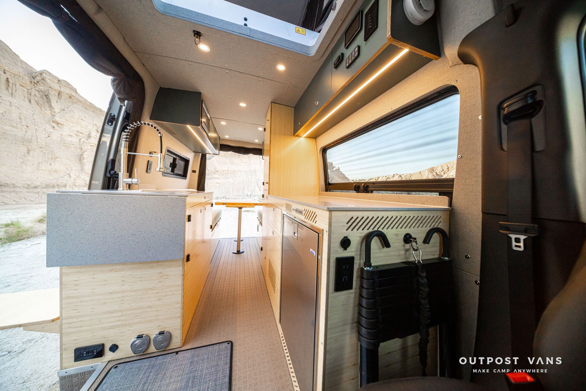 Inside a camper van: minimalist wood interior with sink, countertop, cabinets, and large side window.