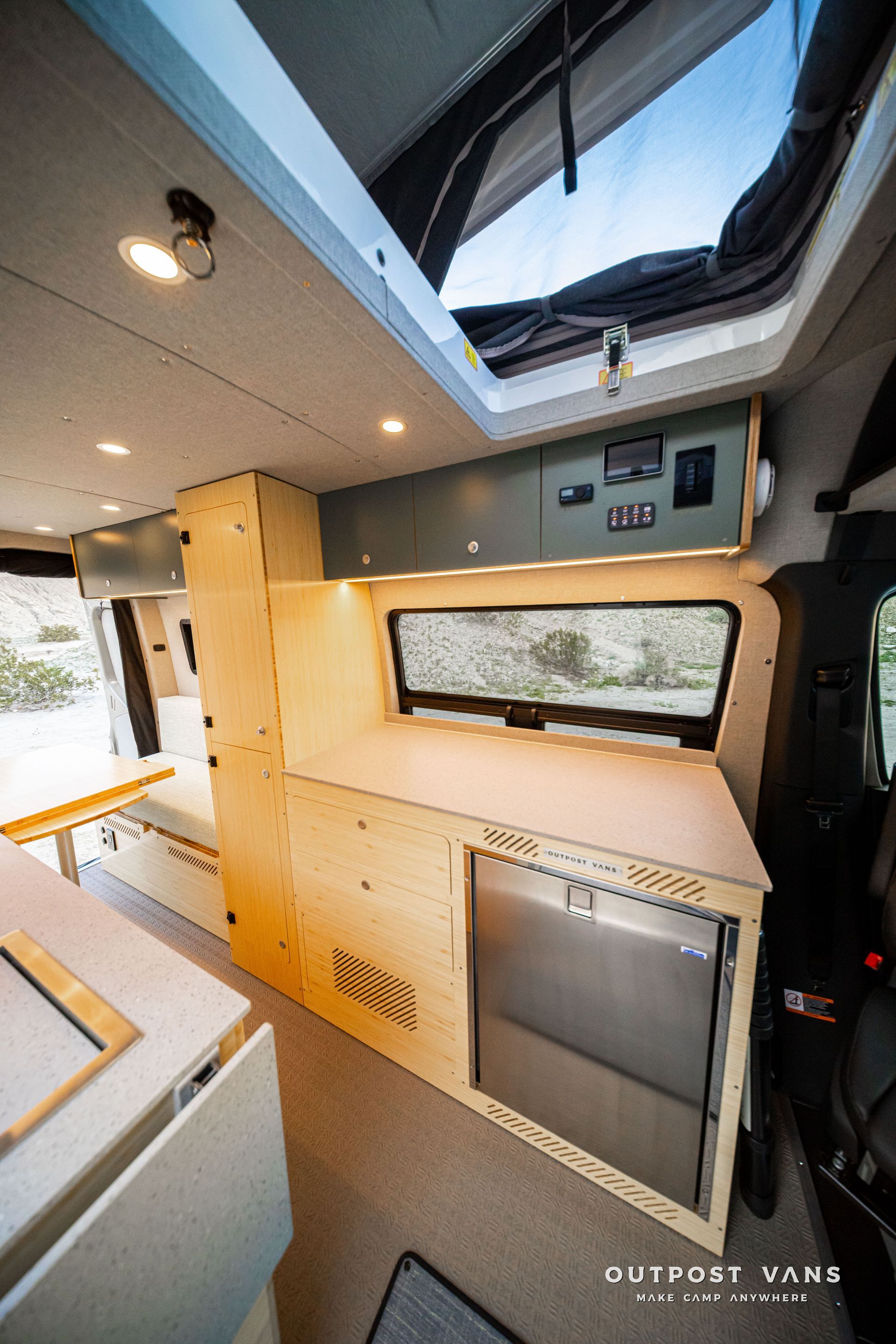 Modern camper van interior with skylight, built-in wooden cabinet, window, and compact kitchen area