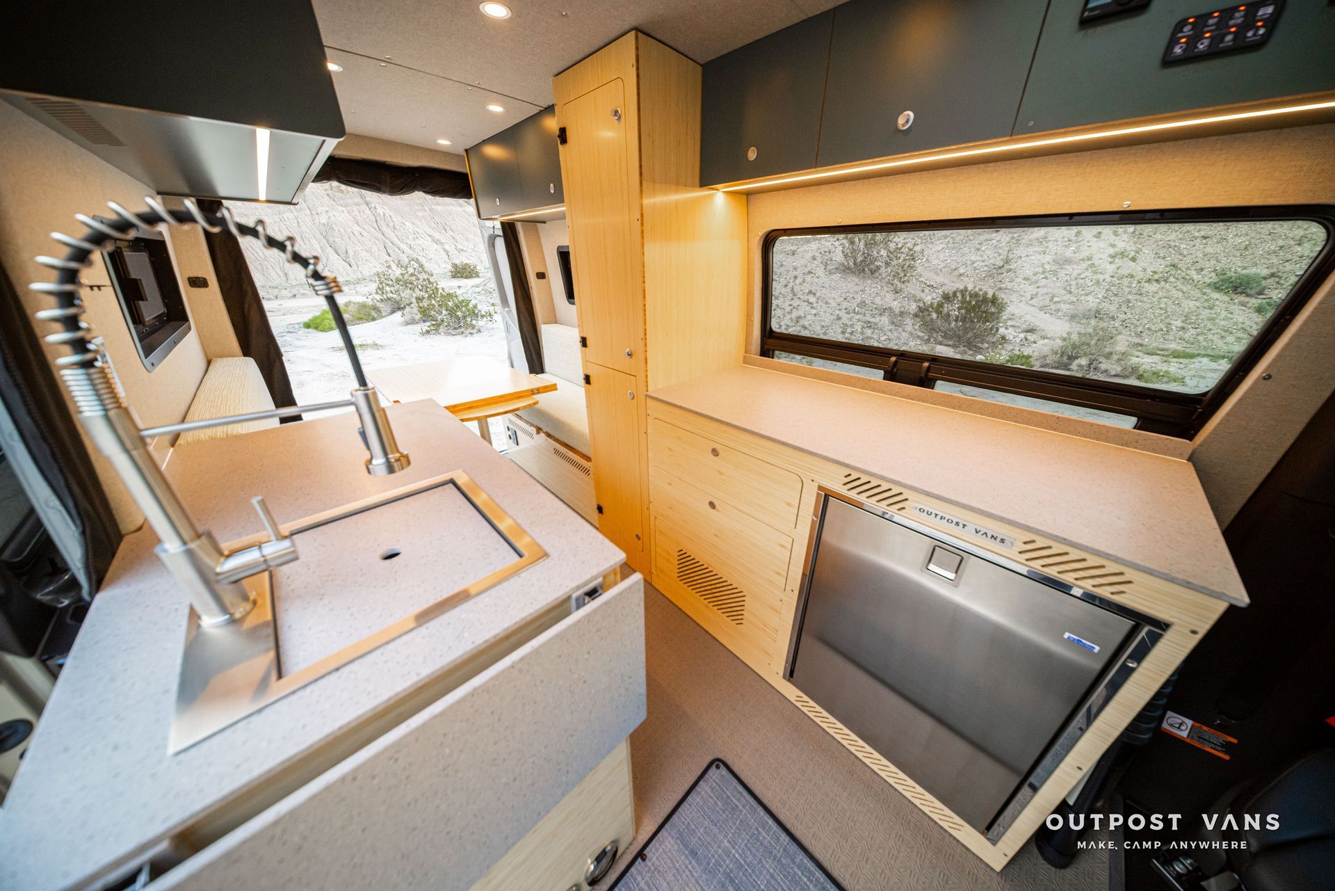 Compact RV kitchen interior with beige cabinets, white counters, sink, and narrow window