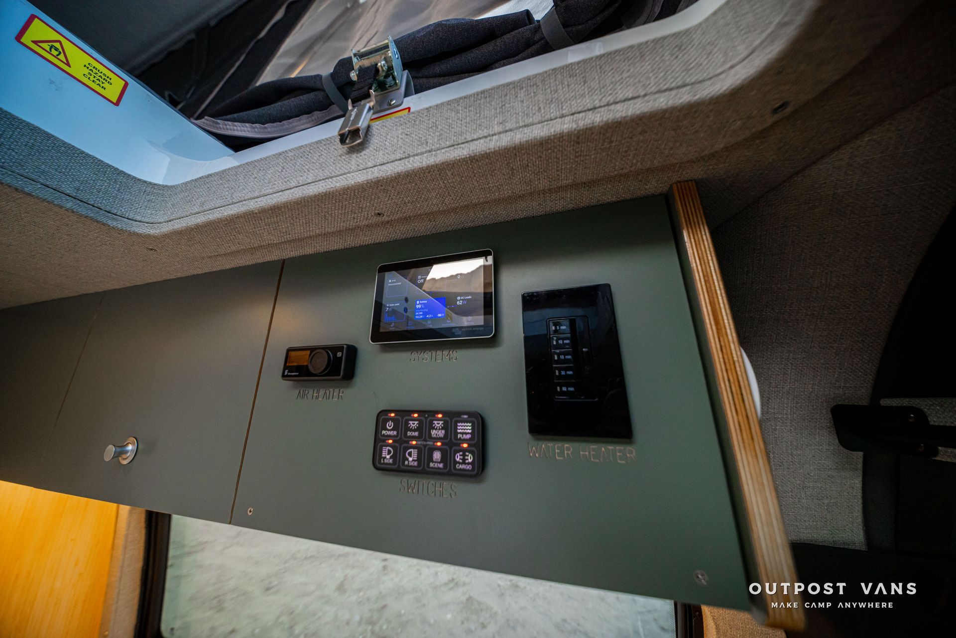 Interior of an RV wall with monitor, control panel, and small display near a window above.