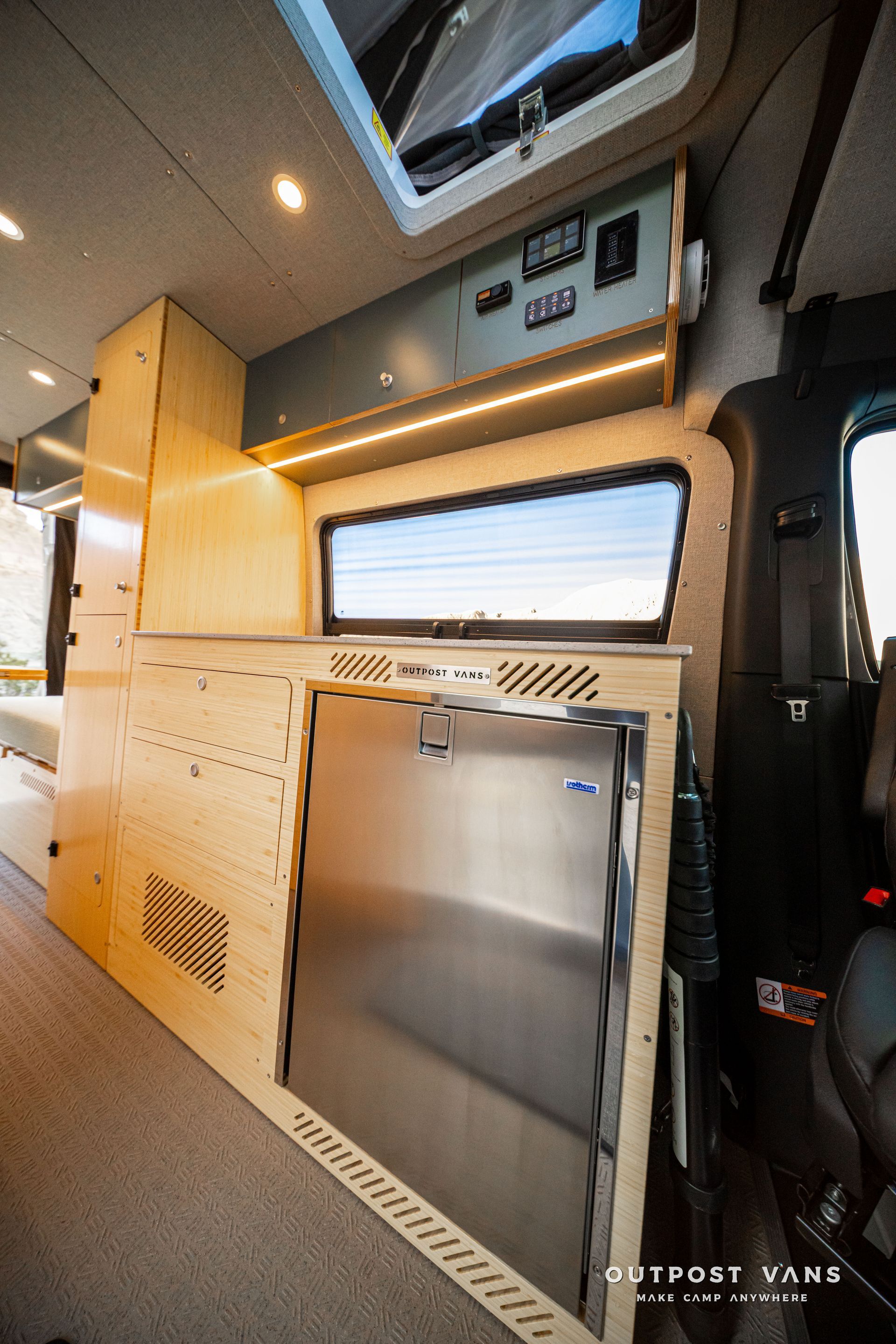 Compact van interior with wood cabinetry, stainless cabinet, and a skylight window.