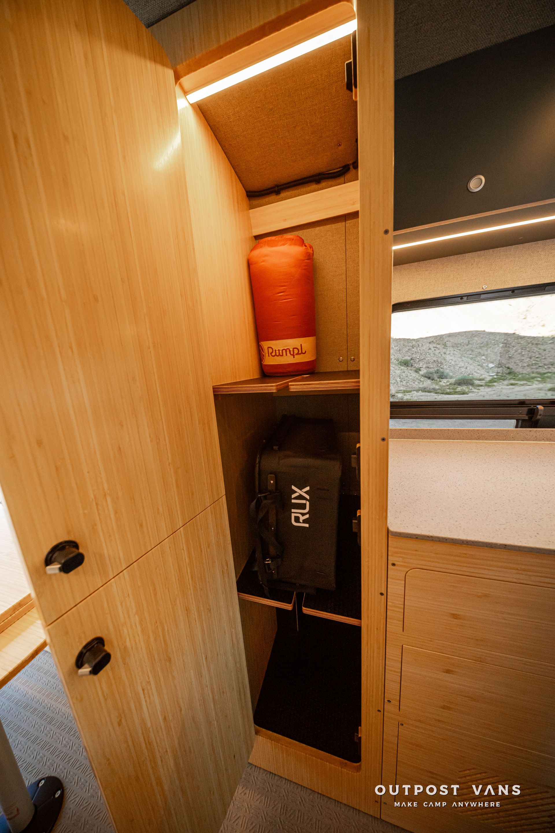 Wooden cabinet with shelves, a black speaker, and a window overlooking greenery.