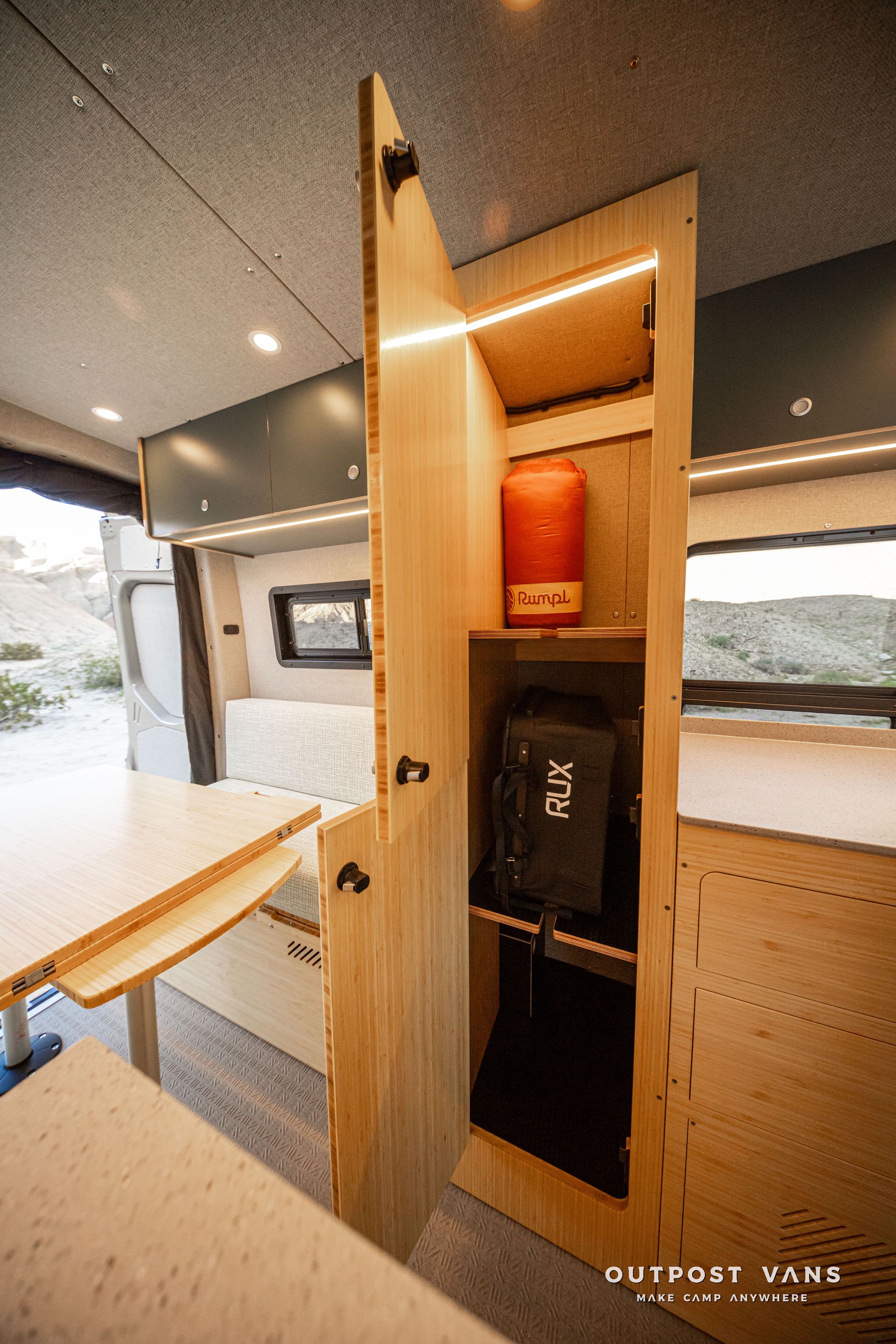 Wooden storage cabinet with shelves holding red and black containers inside a van interior.