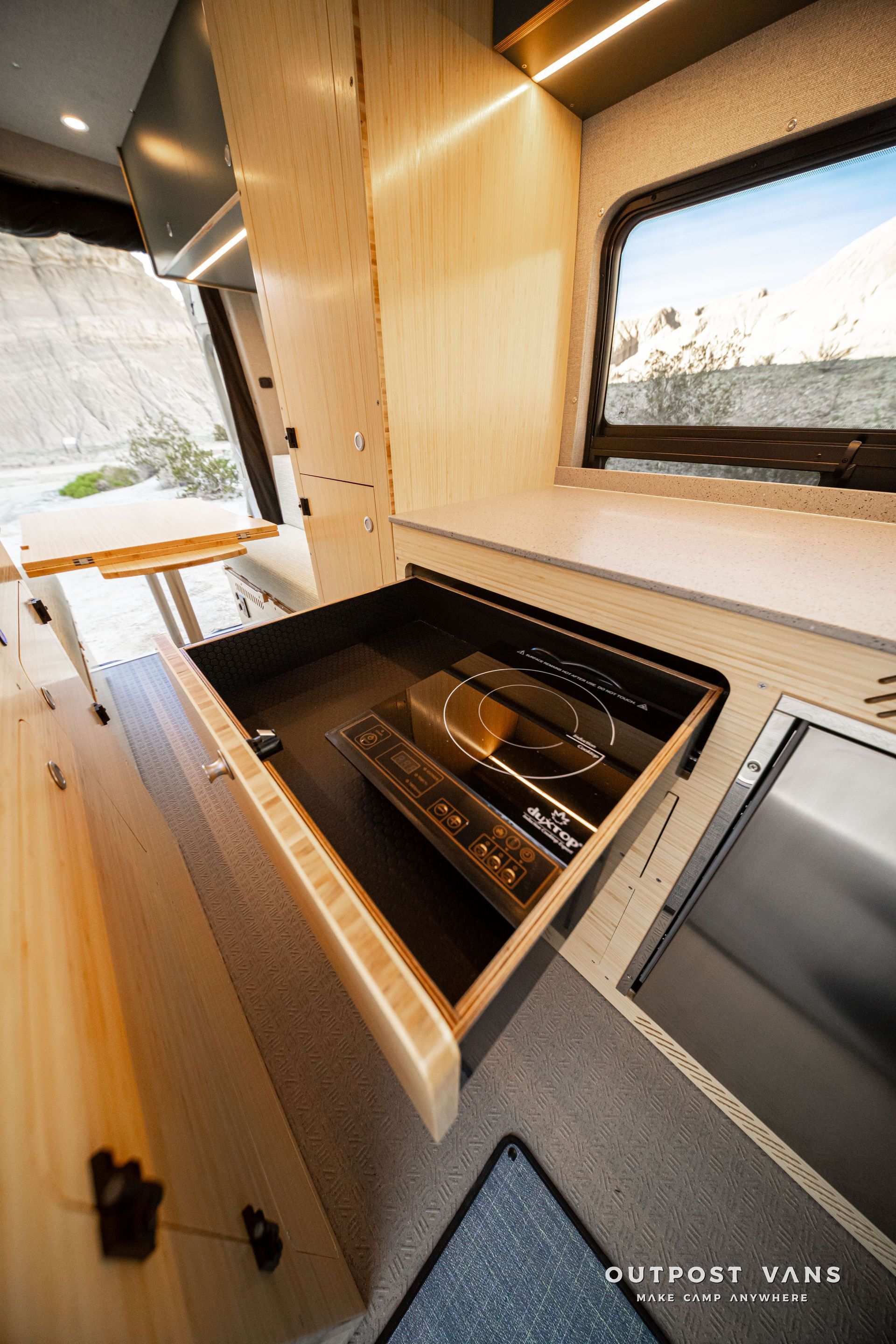 Compact camper kitchen with sink, cooktop, and window over a wood counter