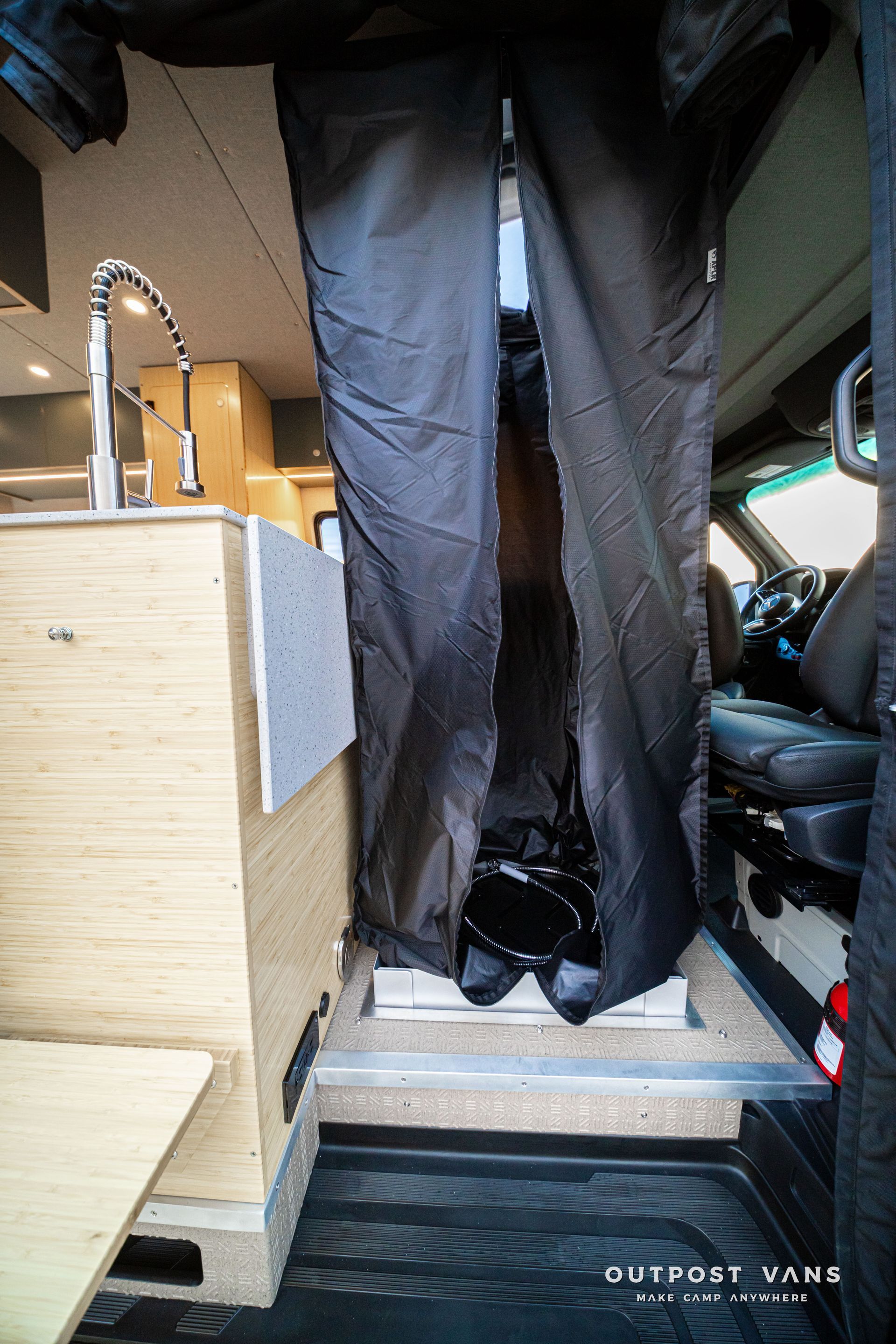Narrow RV aisle with black curtains, wooden cabinet, and a seat visible on the right.