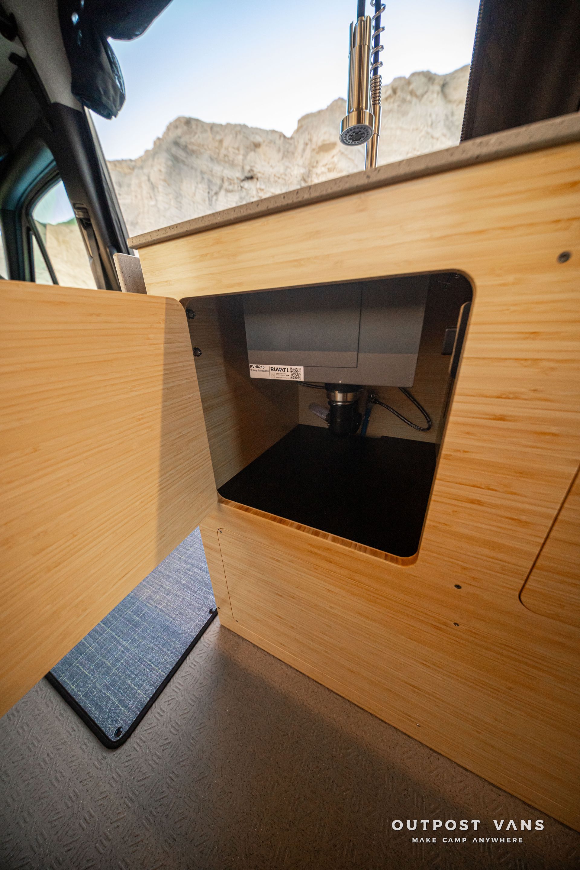 Open wooden cabinet with a dark storage compartment inside a vehicle, with canyon cliffs visible outside.