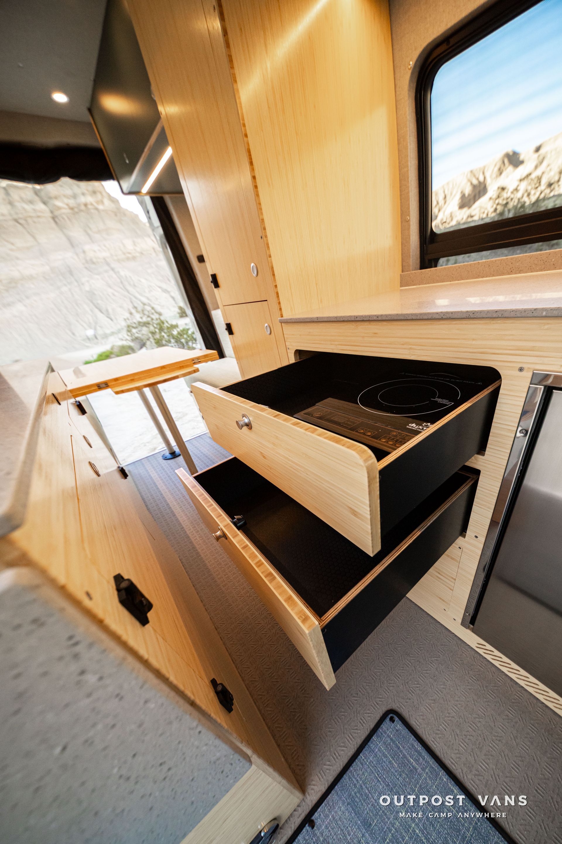 Compact camper kitchen with wood cabinets, sink, black countertop, and window inside a small RV interior