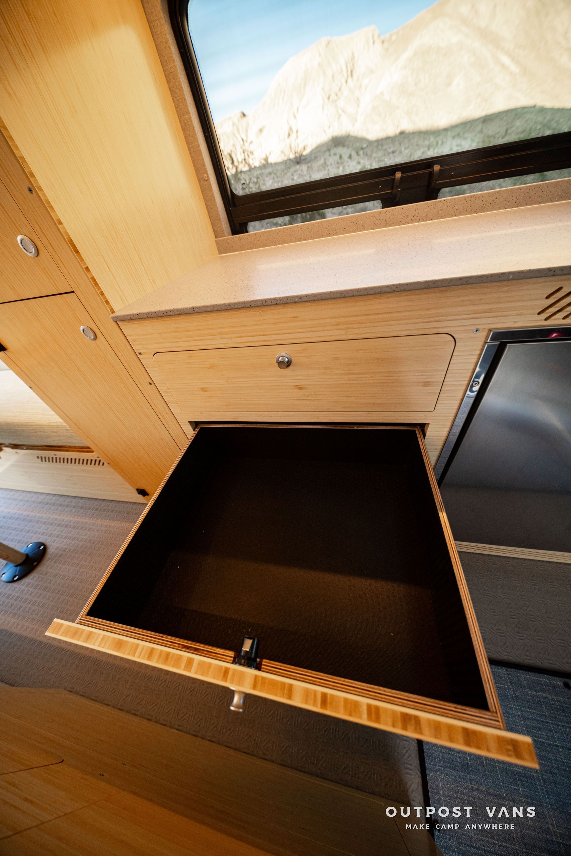 Open wooden storage compartment inside an RV, with a dark empty interior and a nearby window.
