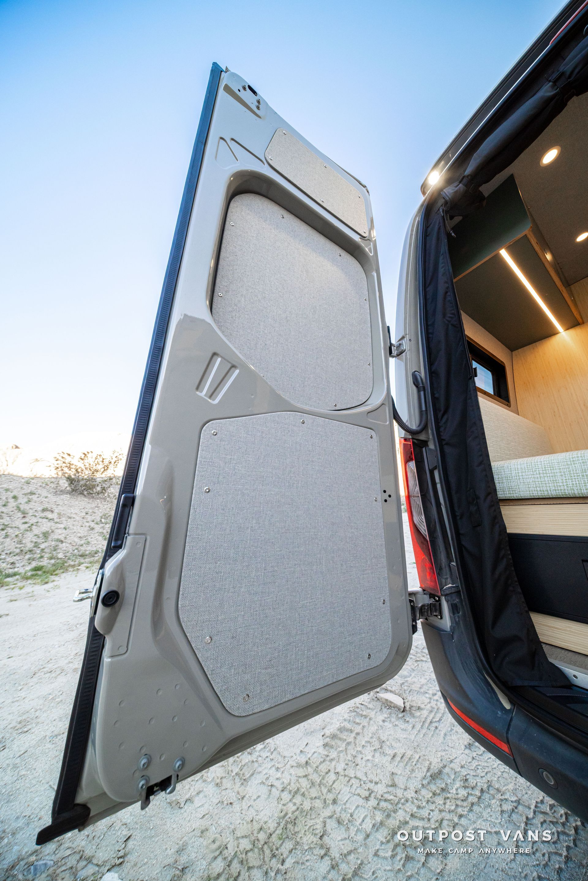 Open rear van door with gray insulated panel and snow outside on the ground