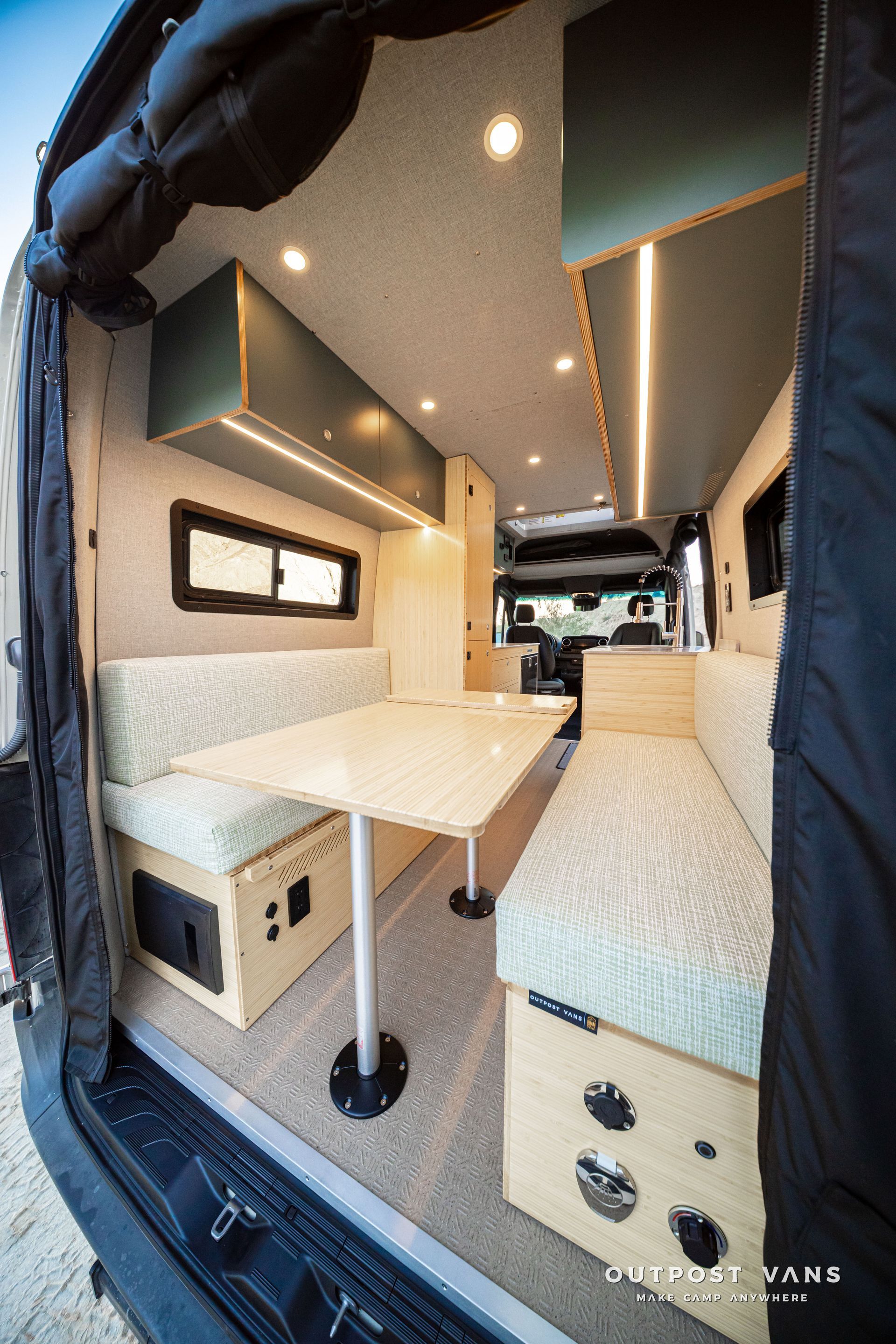 Compact camper van interior with two bench seats, fold-out table, and warm ceiling lights