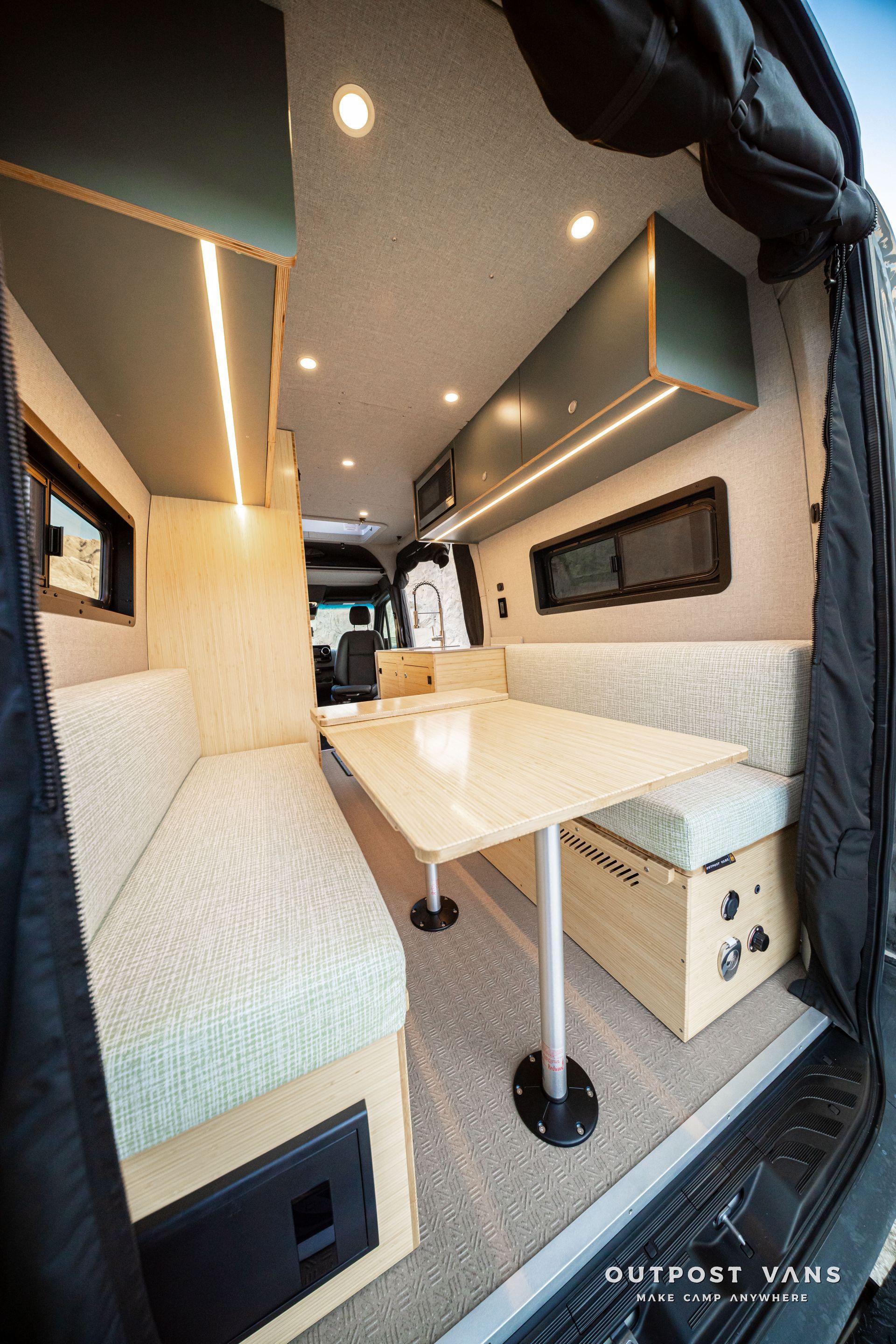 Compact camper van interior with bench seats, fold-out table, and overhead lights