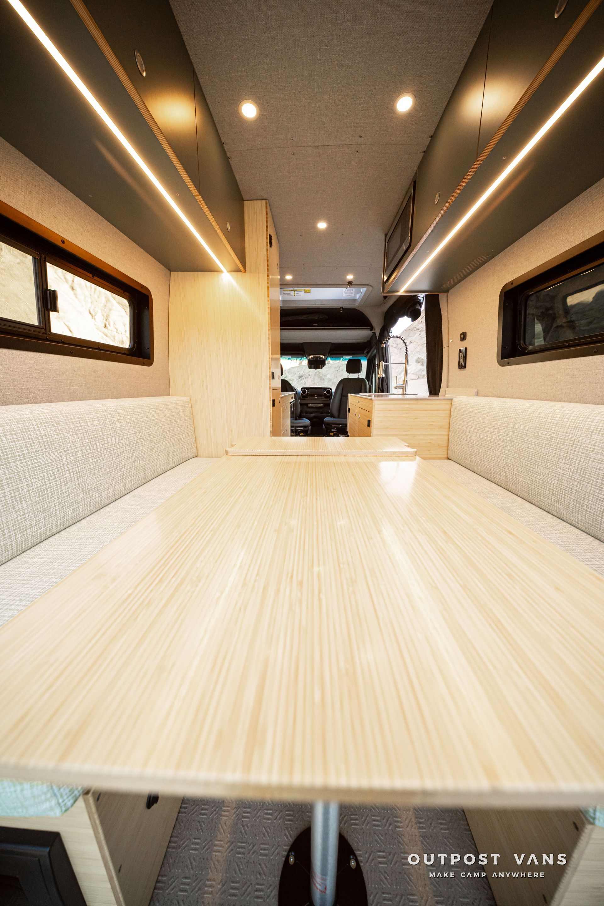 Interior of a compact RV camper with a wood table, cushioned benches, and warm ceiling lights