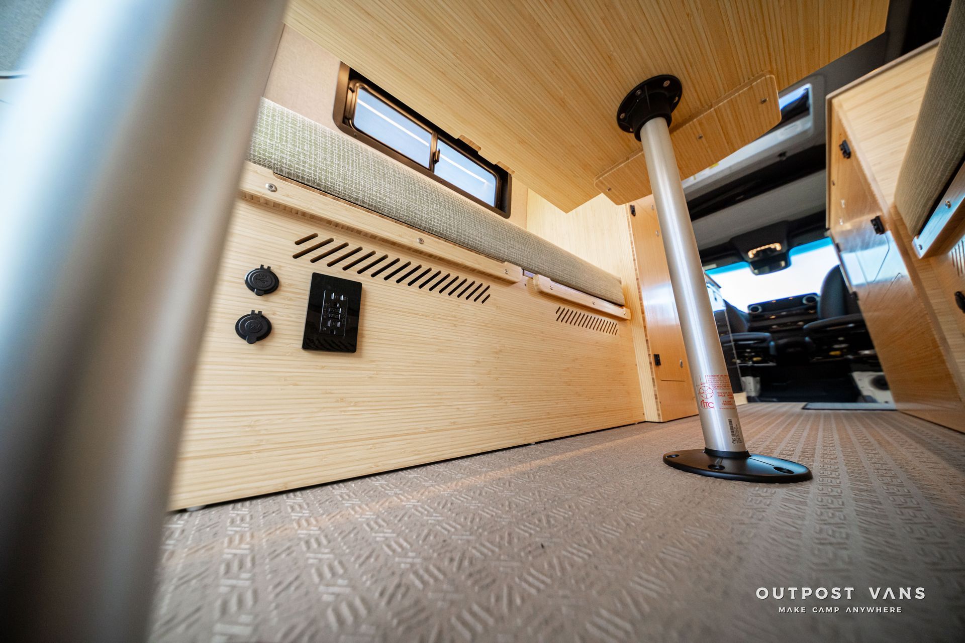 Interior of a van with wood paneling, carpeted floor, and a central pole near a side window.