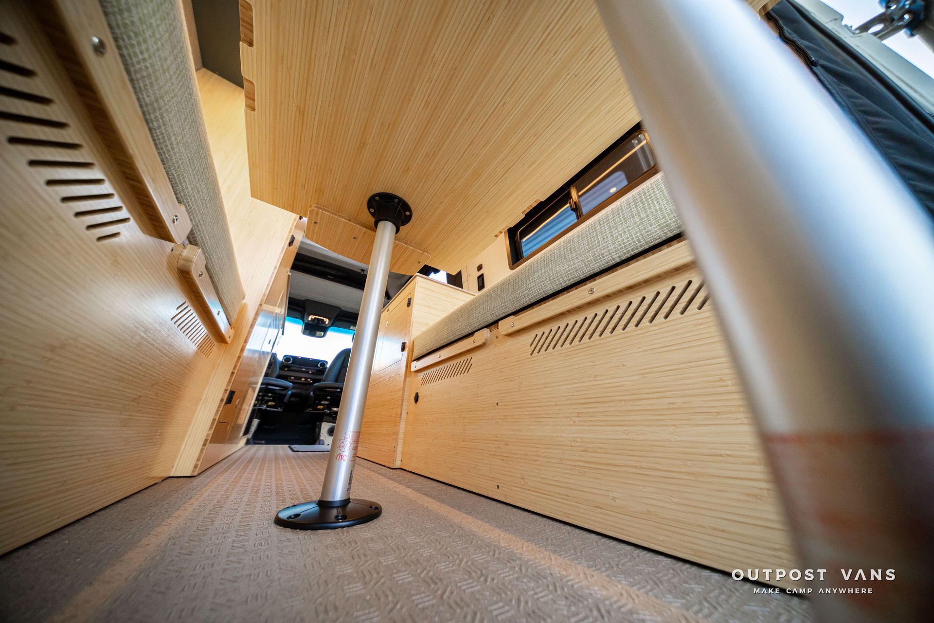 Low-angle view under a train seat, showing metal poles and carpeted floor.