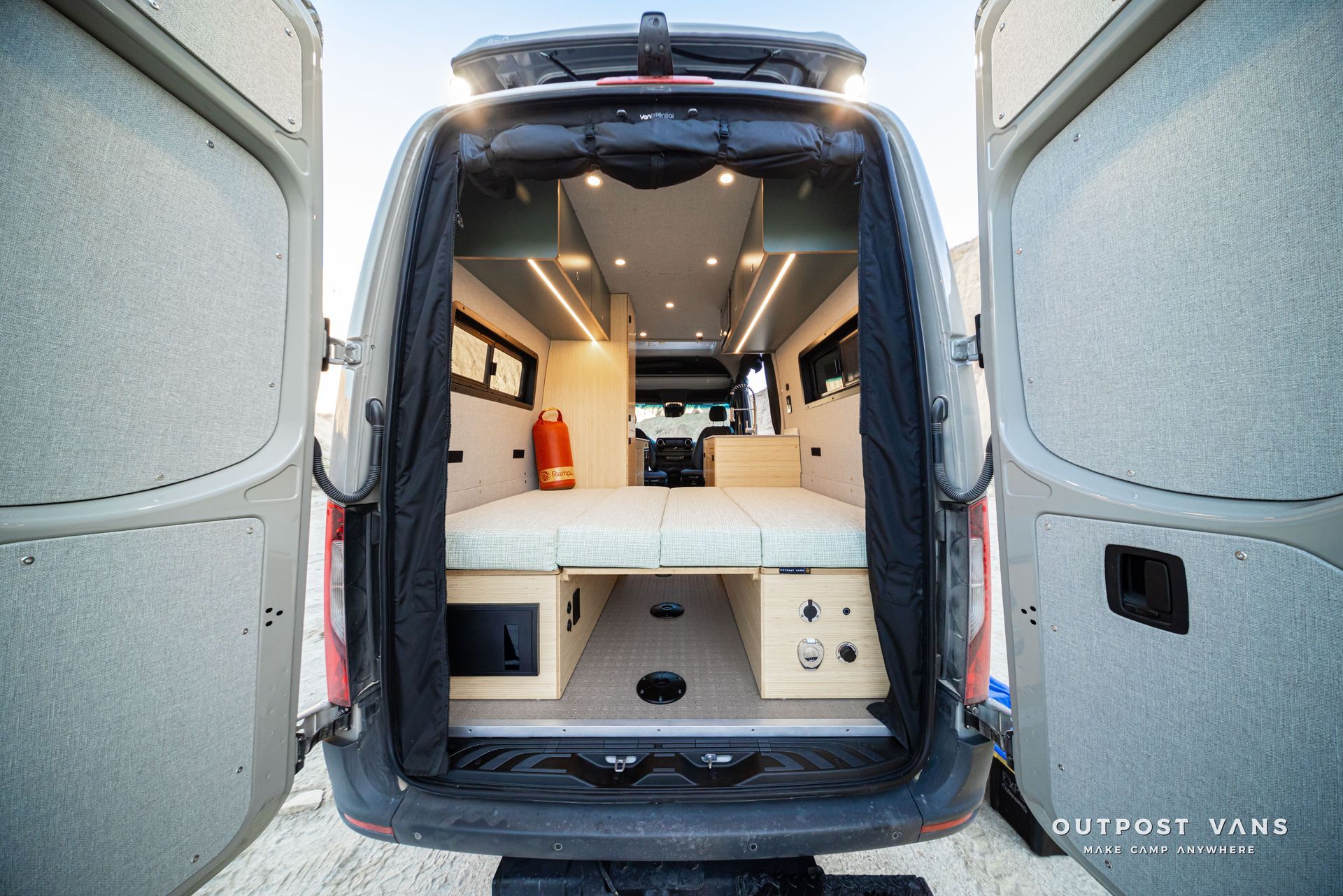 Open cargo van converted into a compact camper with bed, cabinets, and ceiling lights
