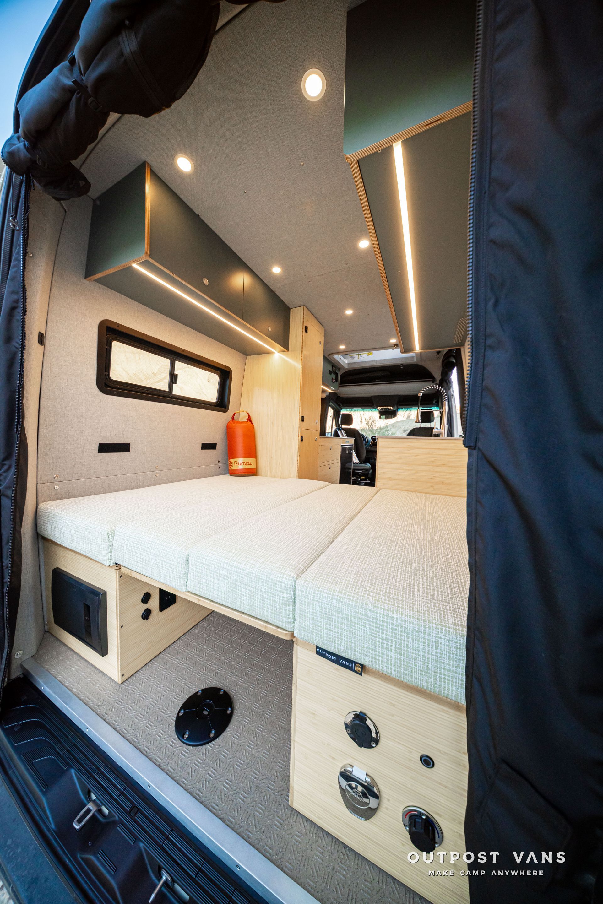 Compact camper van interior with white bed platform, cabinets, skylight, and front cab visible