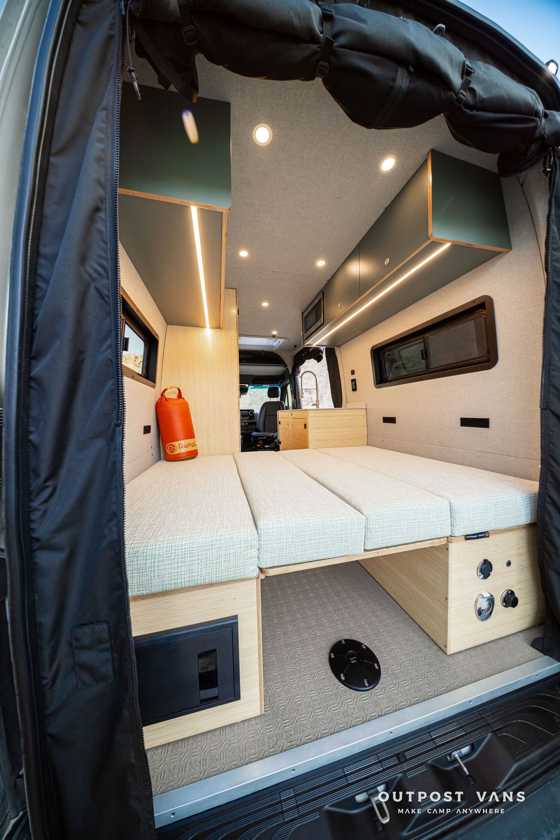 Compact camper van interior with bed platform, overhead lights, and wood storage cabinets
