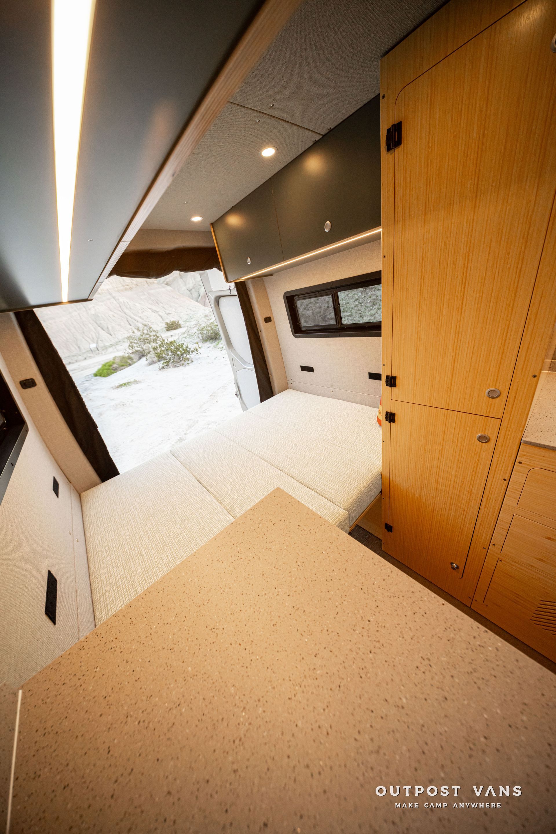 Modern tiny bedroom with built-in wood cabinetry, skylights, and a snowy view through a large window.