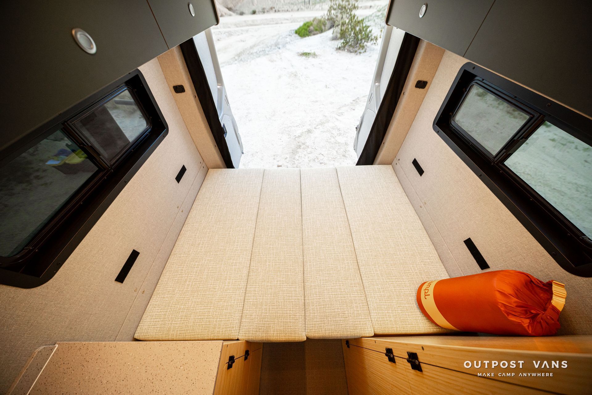 Interior of a vehicle with open rear doors, showing a light carpeted cargo area and snow outside.