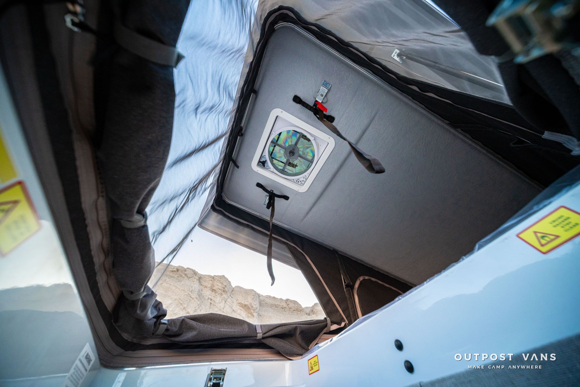 Looking up through a torn tent roof toward a hanging square panel with a green emblem.