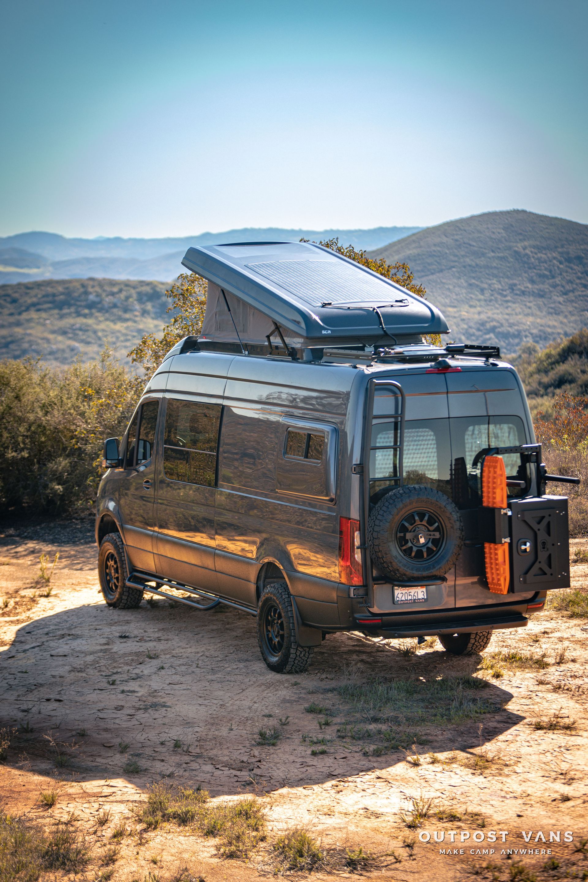 a van with a tent on top of it is parked on top of a dirt hill .